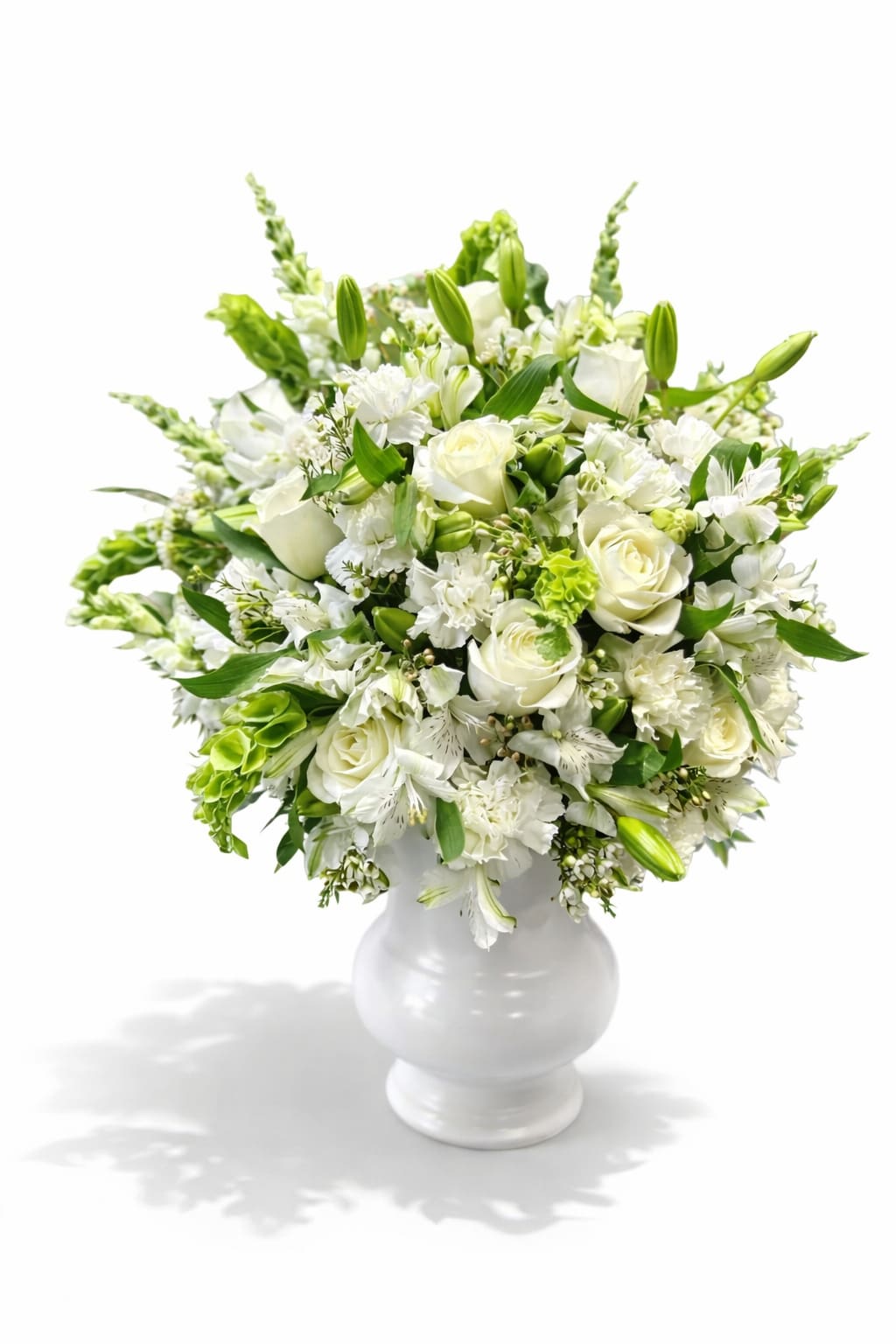 Angelic White Urn - White roses, lilies, snap dragons and carnations with bells of Ireland and alstromeria arranged in a white urn style plastic container. Custom script can be requested in the notes if desired  **When crafting floral arrangements, we aim to replicate the image as closely as possible. Remember, each design is one-of-a-kind and tailored specifically for you. Given the characteristics of flowers, some color adjustments may be necessary. Additionally, the prices and availability of seasonal blooms can vary