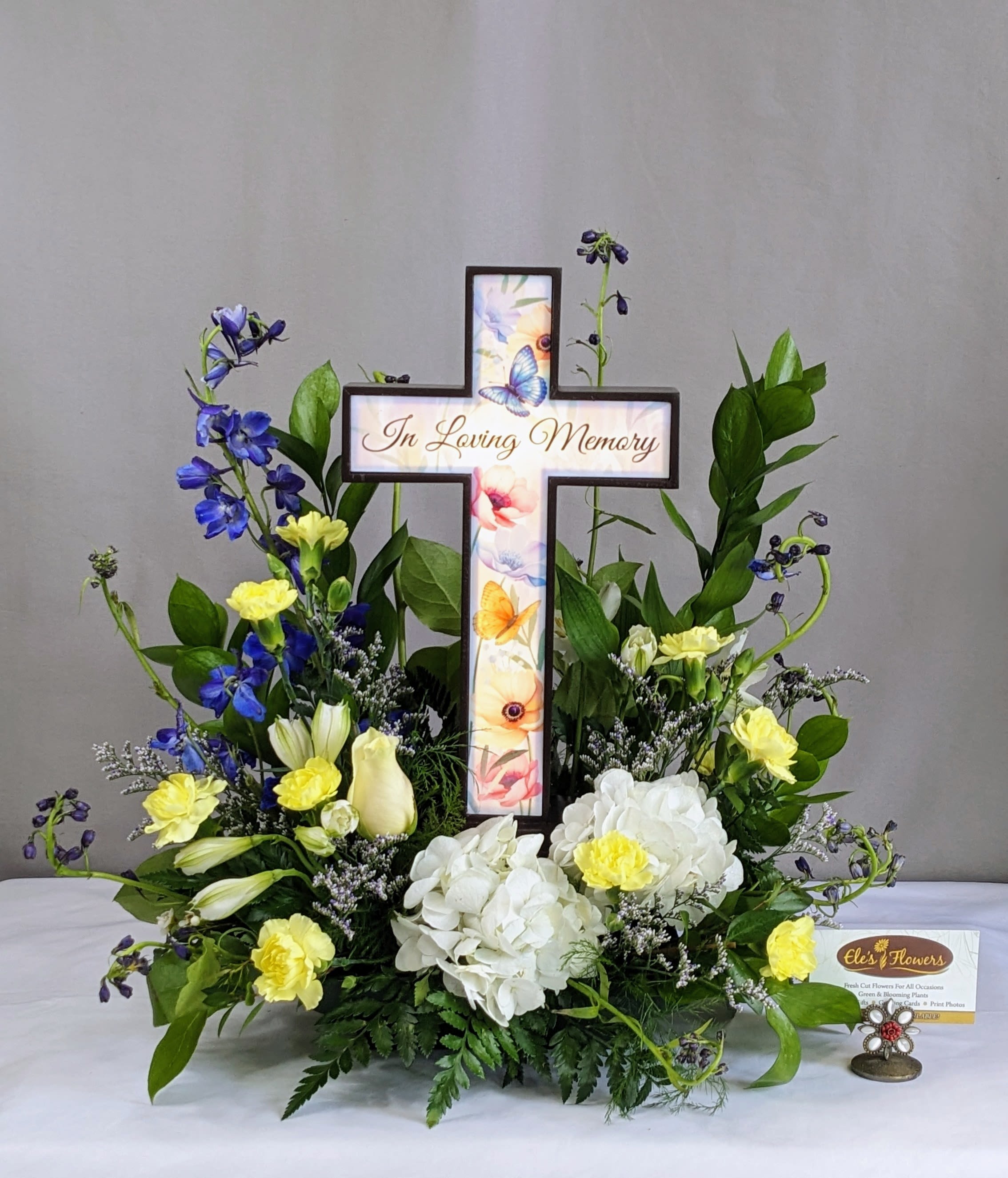 Memorial floral cross with white and yellow flowers and blue accents
