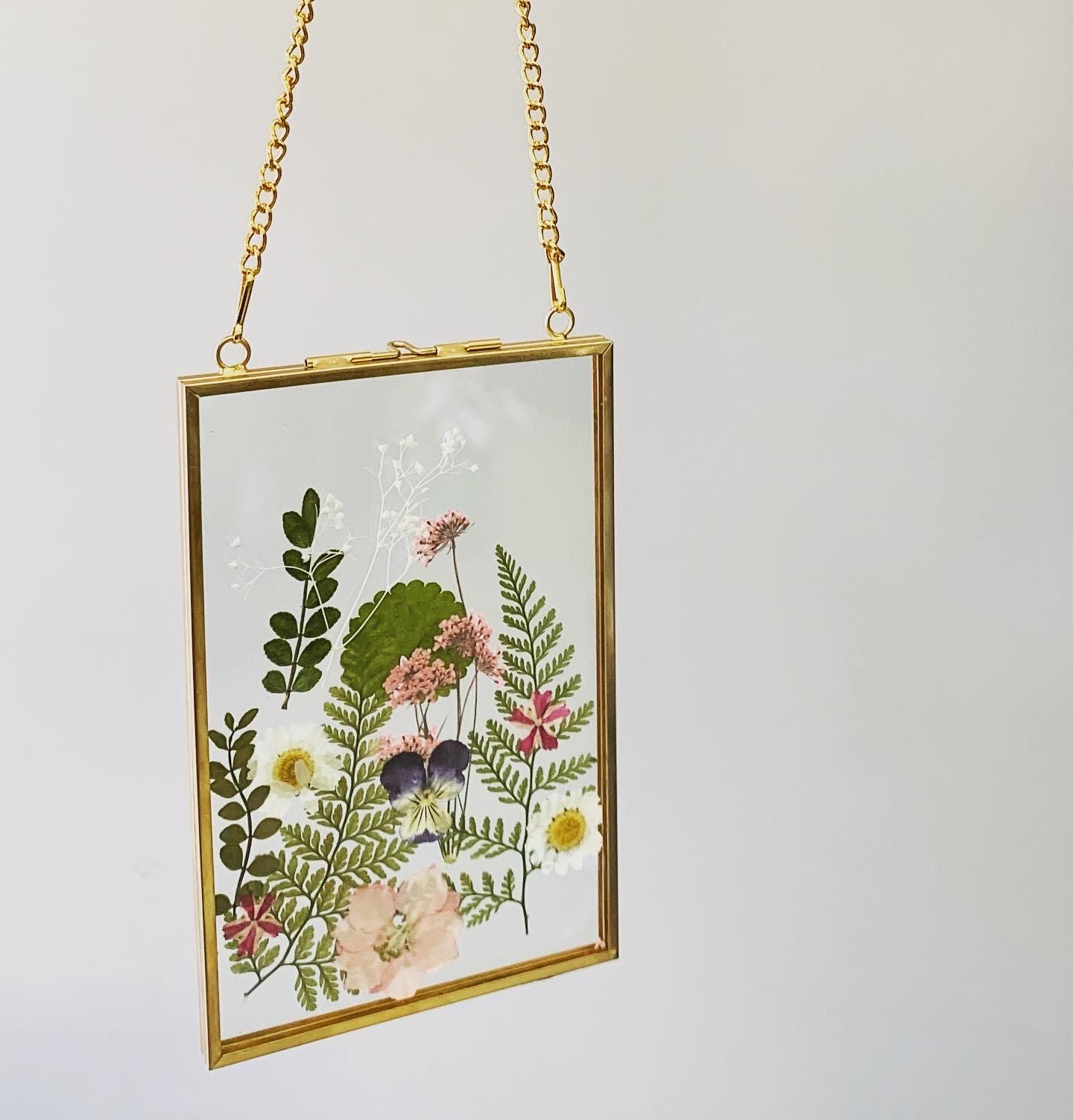 Pressed flowers in a gold hanging frame with a chain