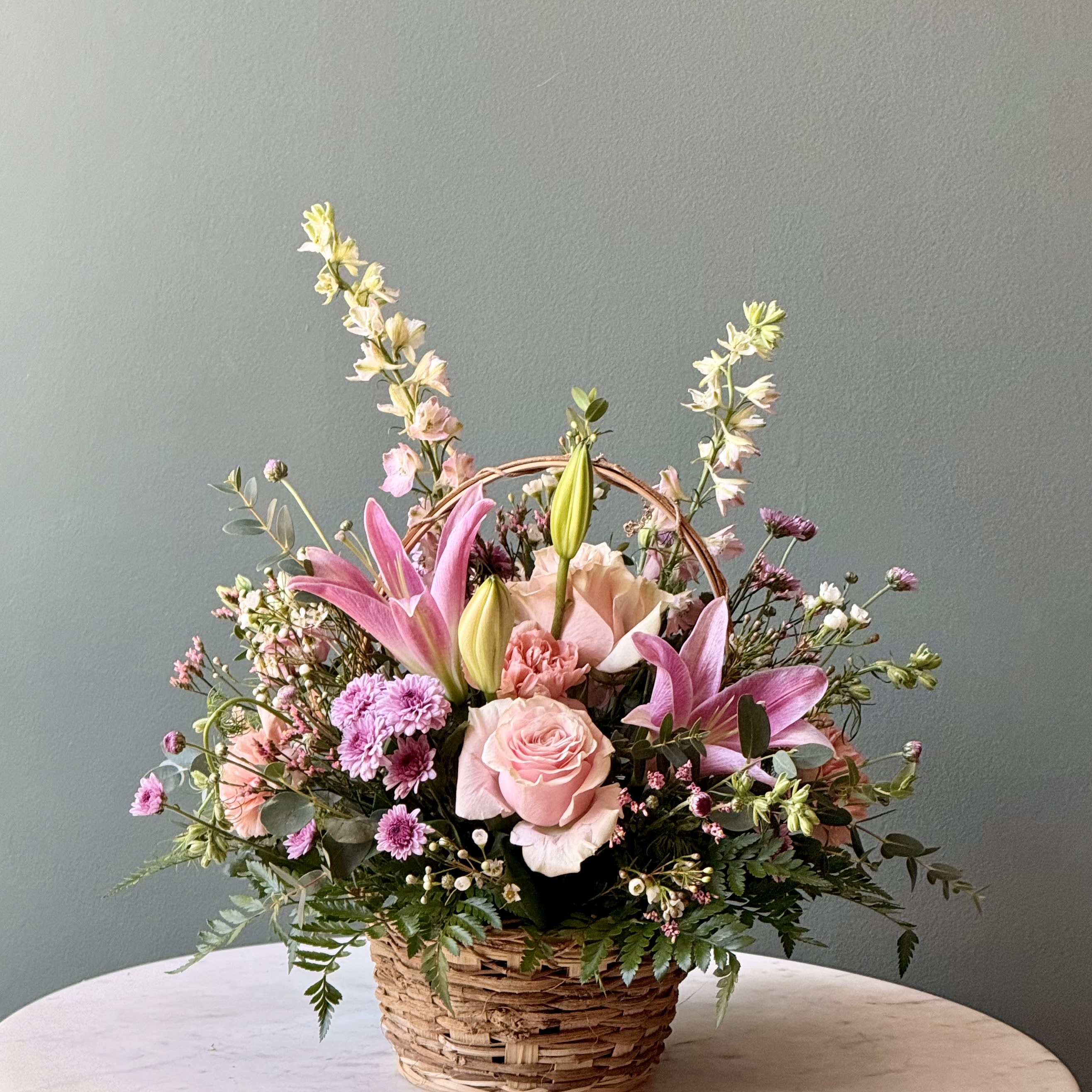 Pink lilies and roses arranged in a wicker basket