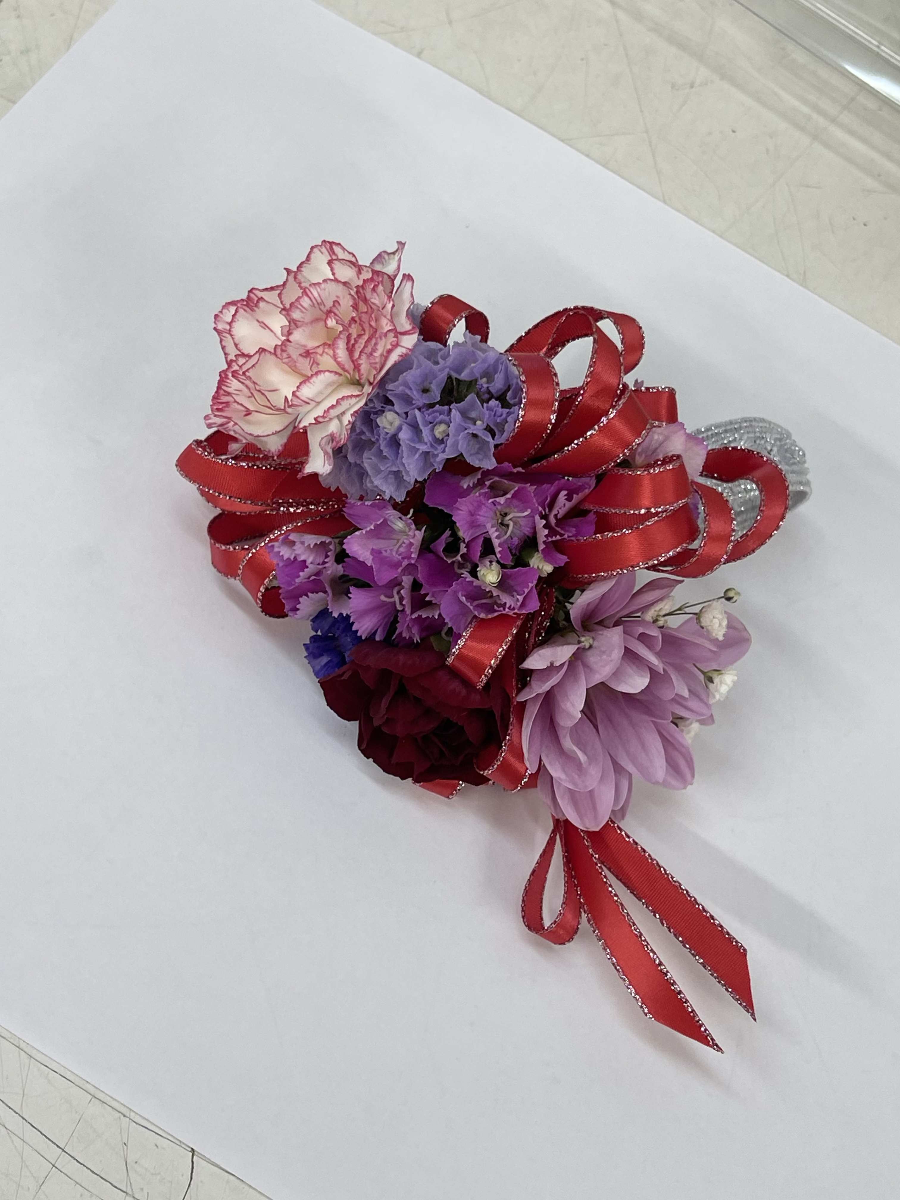 Small corsage with pink, purple, and burgundy flowers tied with red ribbon