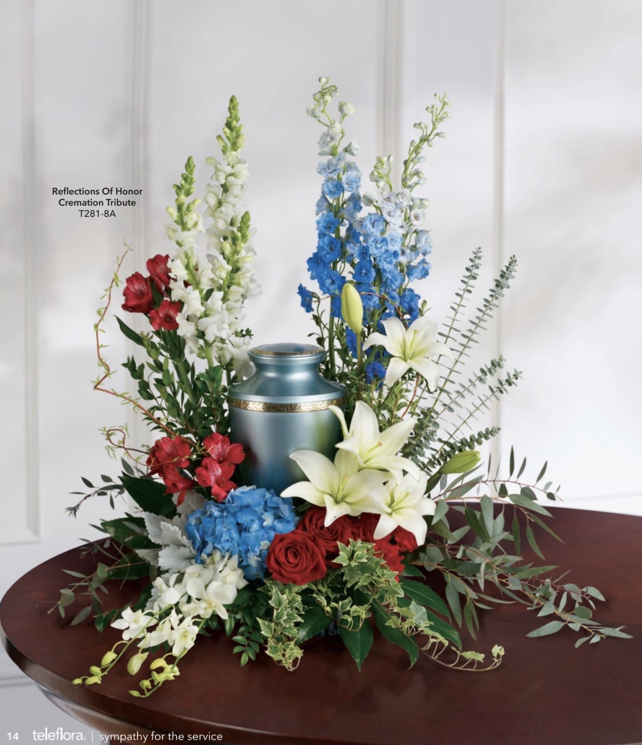 Reflection Of Honor Cremation - A dignified, ceremonial tribute that honors a life with quiet strength and patriotic grace - this cremation flower arrangement and urn is a thoughtful sympathy piece for a funeral or memorial service. The design centers on a blue ceramic urn and is arranged as a formal, upright spray suited for a cremation tribute, offering a respectful way to mark a service and let the person you're thinking of feel remembered.  Layered vertical movement rises from a low base of red and white roses, blue hydrangeas, and creamy lilies into taller spikes of snapdragons, alstroemeria and stems of dendrobium orchids. The palette of blue, white, red and green is restrained and ceremonial; clustered blooms and textured foliage create a composed, full presentation that reads as both patriotic and intimate. The ceramic urn is integrated into the design, making this a complete memorial expression.  Perfect for a funeral service, graveside ceremony, or as a lasting tribute left with a family, this arrangement conveys respect and honor without overwhelming. Because it's built for cremation use, the piece arrives ready to display at the service; standard care for the blooms-fresh water and a cool location out of direct sun-will help flowers look their best for the occasion.