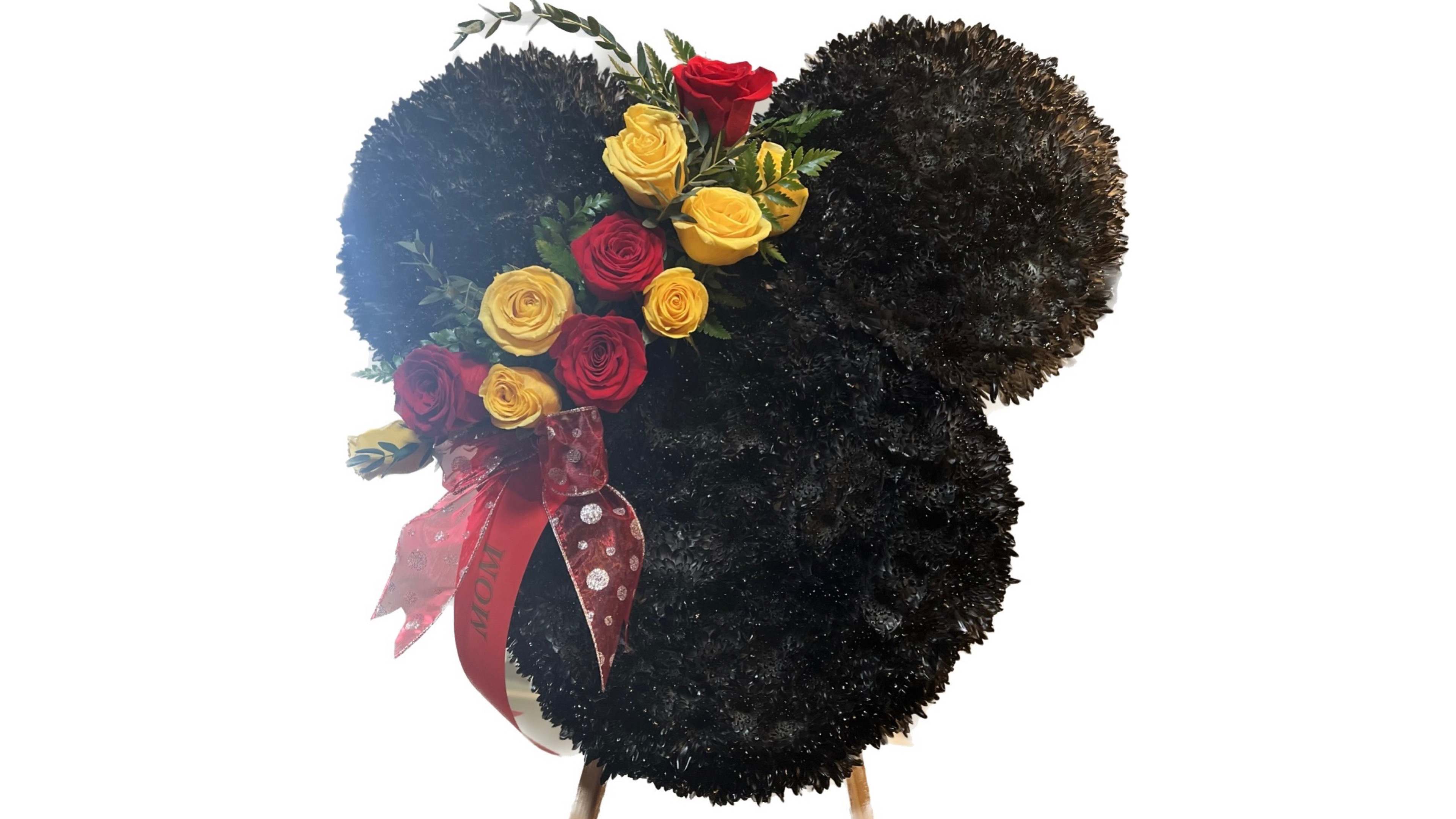 Mouse-ear shaped black floral wreath with red and yellow roses and a red MOM ribbon.