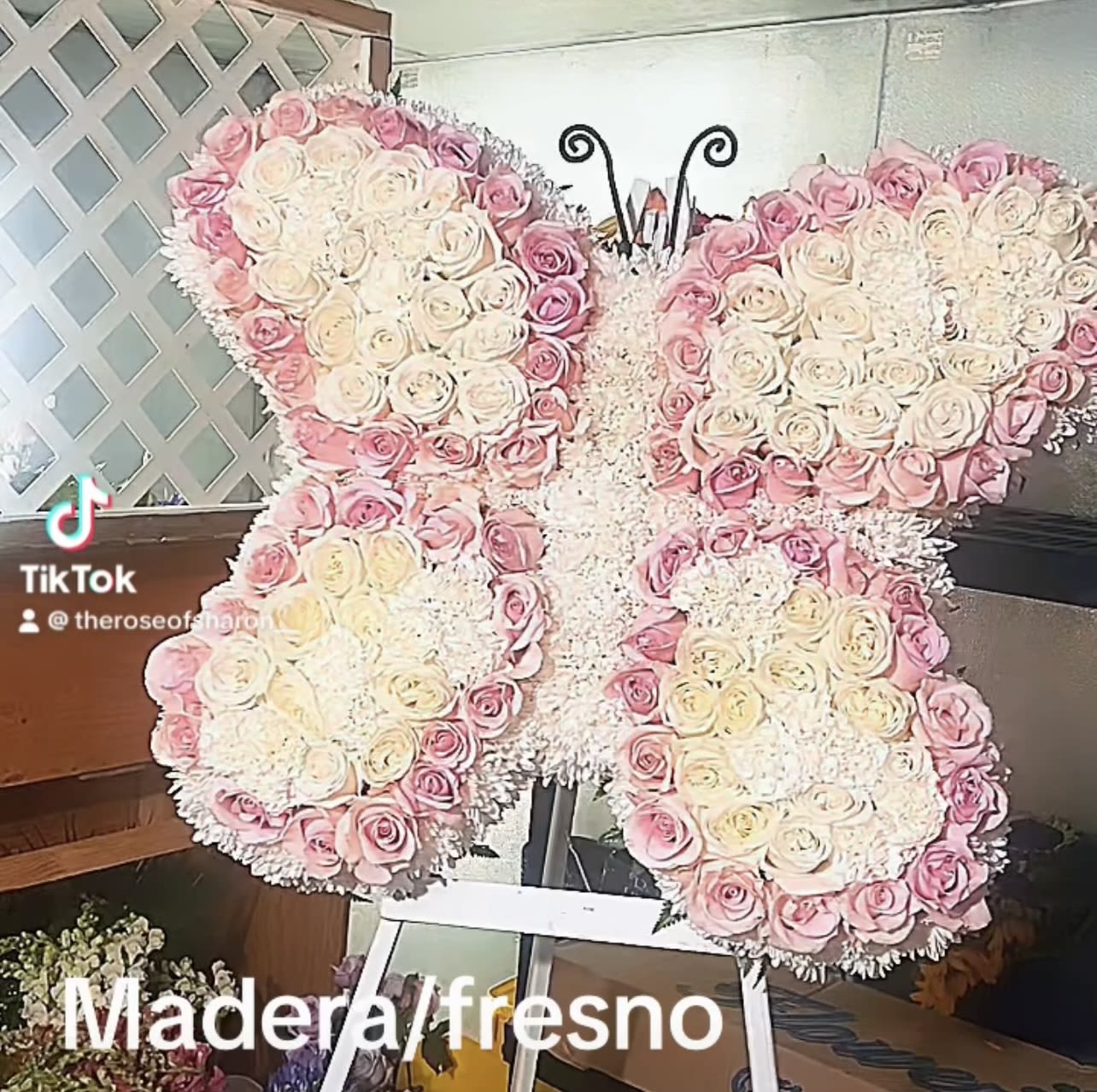 Butterfly-shaped floral arrangement of pink and white roses on an easel