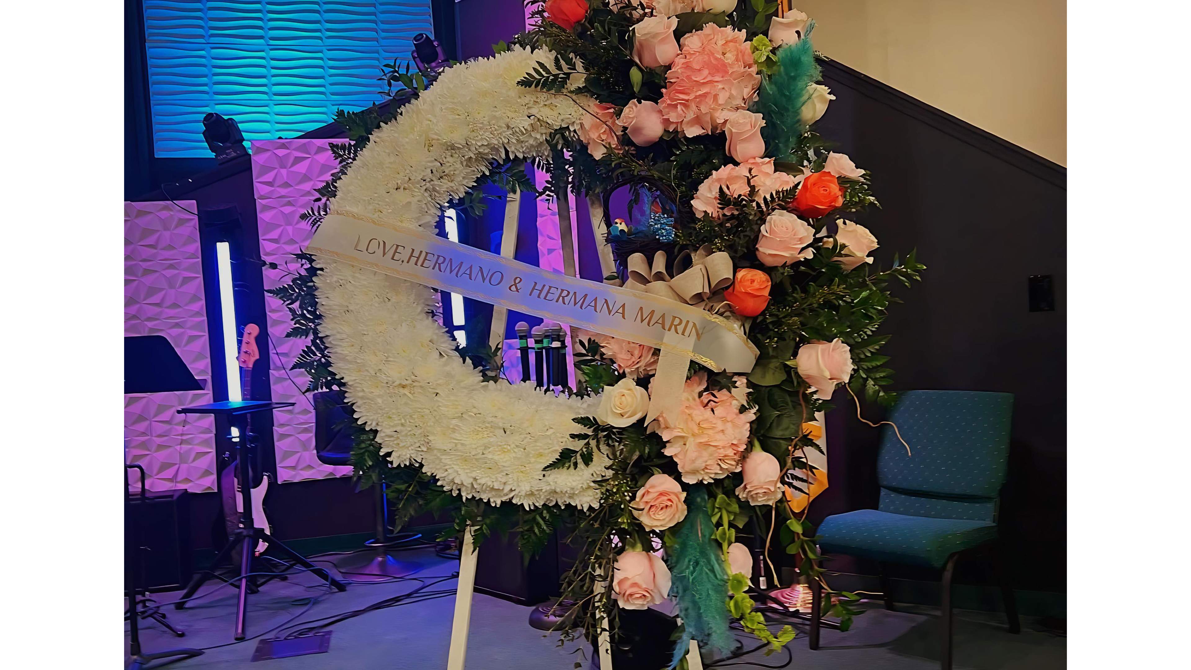 Large crescent-shaped white standing wreath with pink and orange roses on an easel indoors