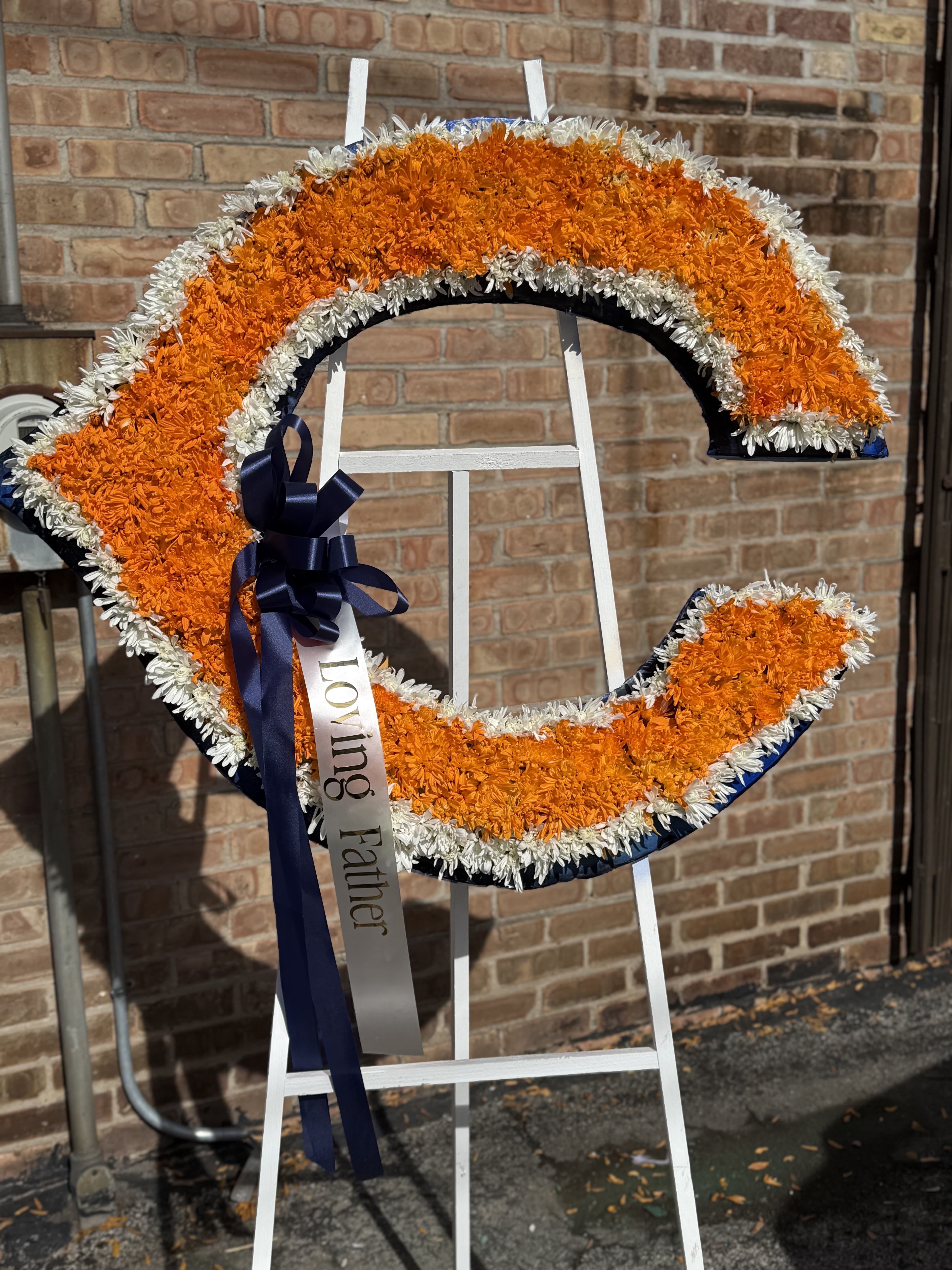Orange and white floral funeral wreath on a stand with a ribbon