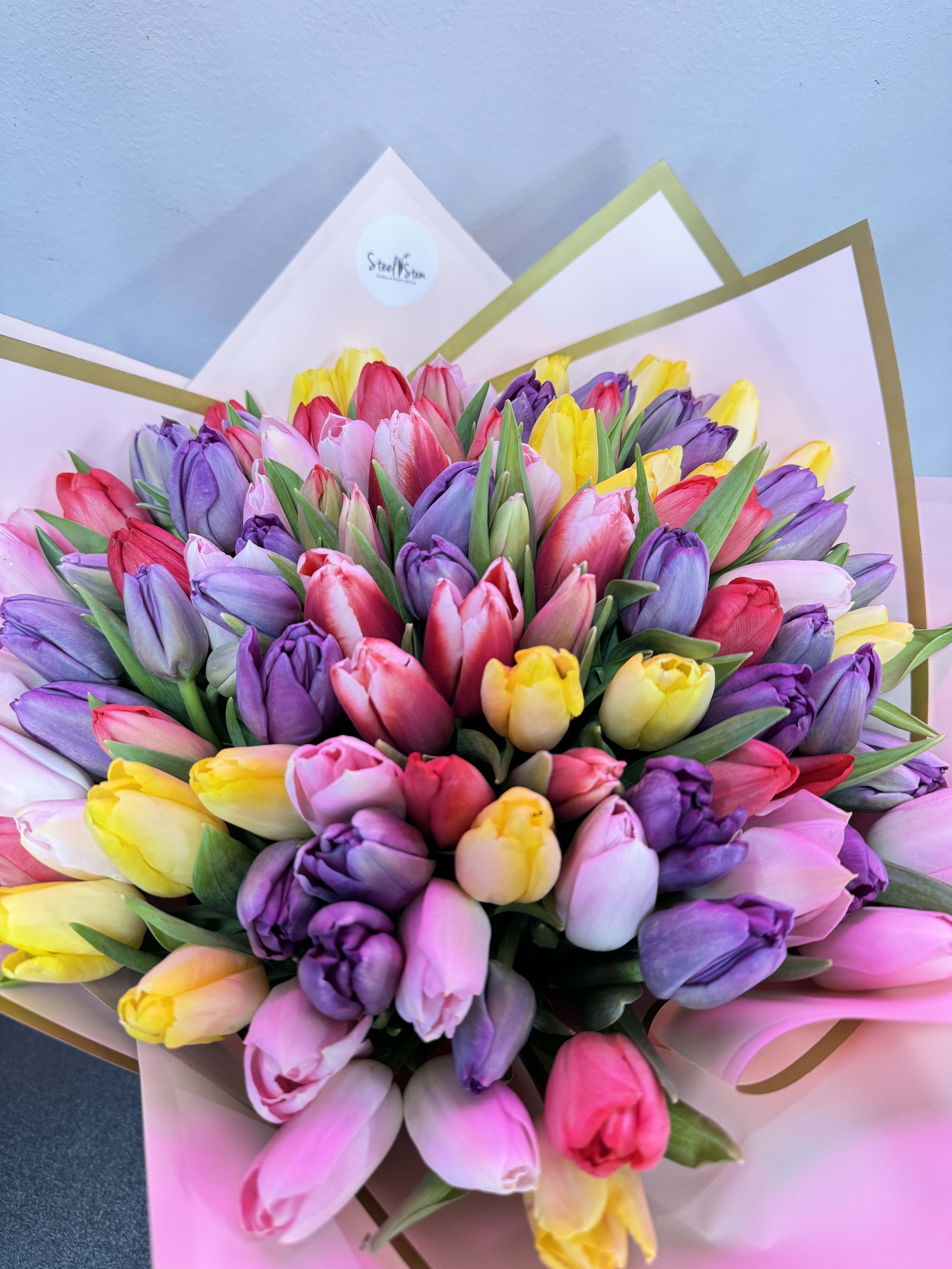 Hand-tied bouquet of multicolor tulips wrapped in pink paper with gold-edged folds
