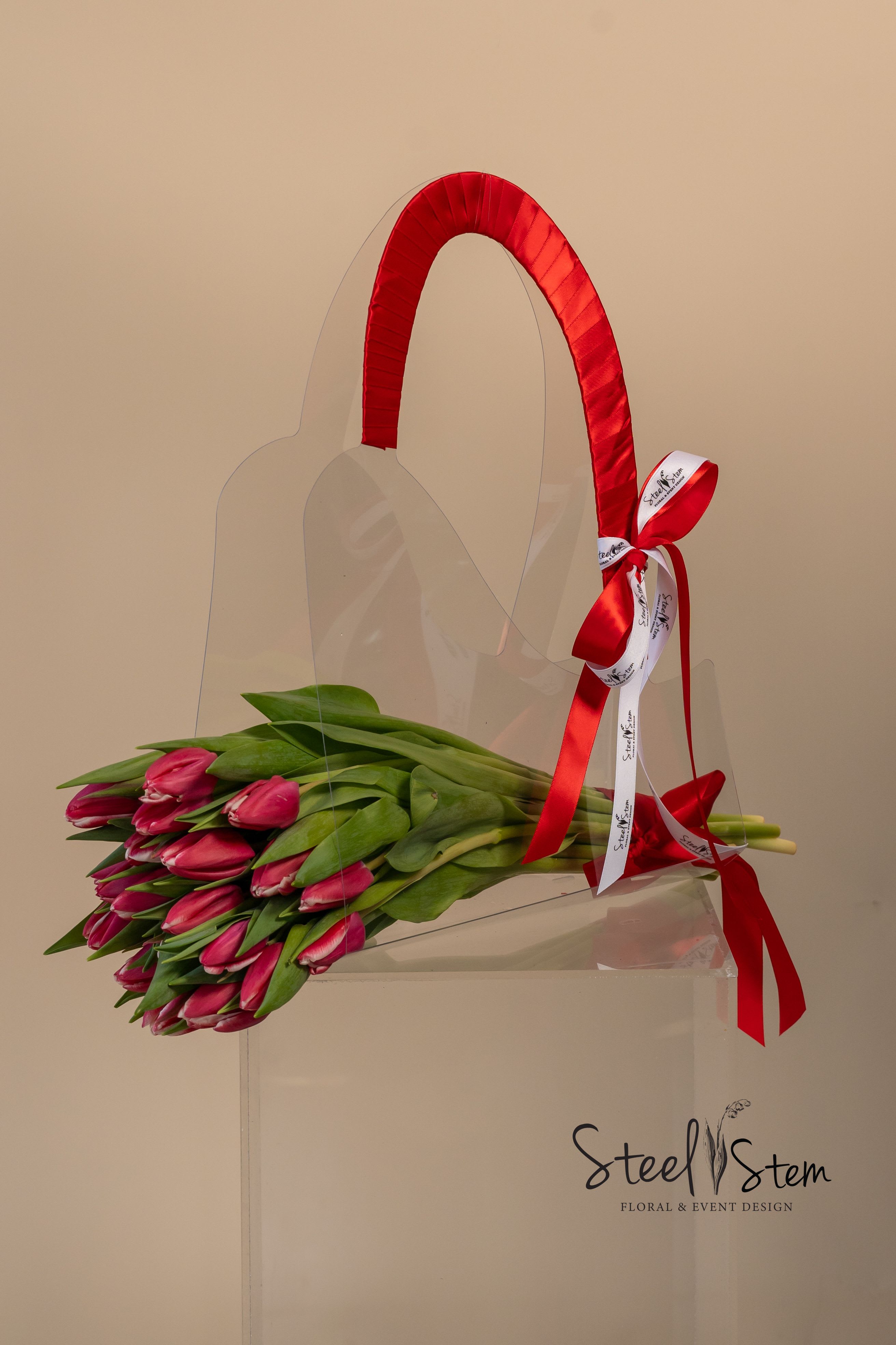 Bundle of pink tulips in a clear tote with a red ribbon handle