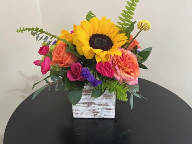 Bright sunflower and mixed roses in a whitewashed wooden cube vase