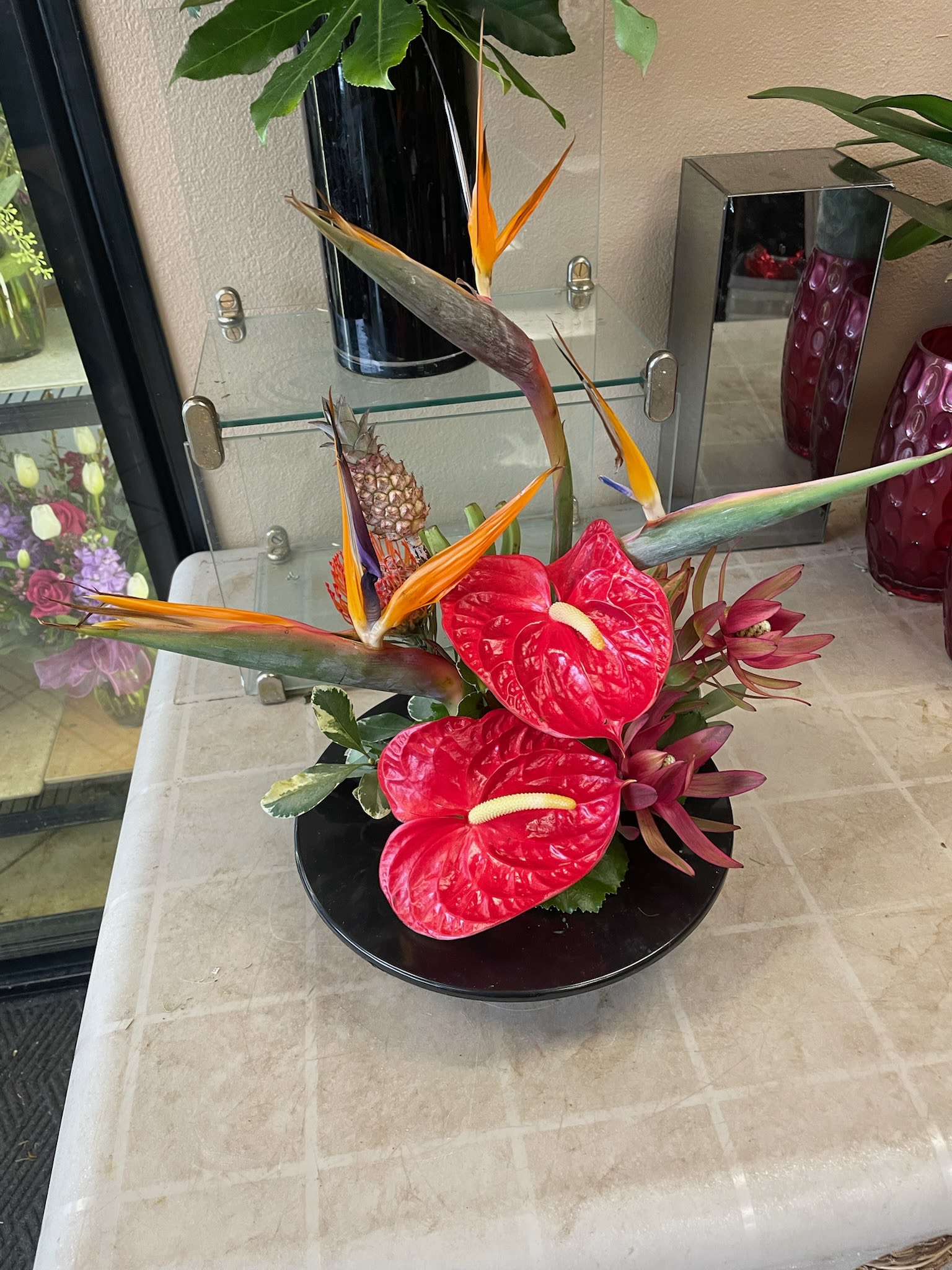 Tropical arrangement with red anthuriums and bird of paradise in a black bowl