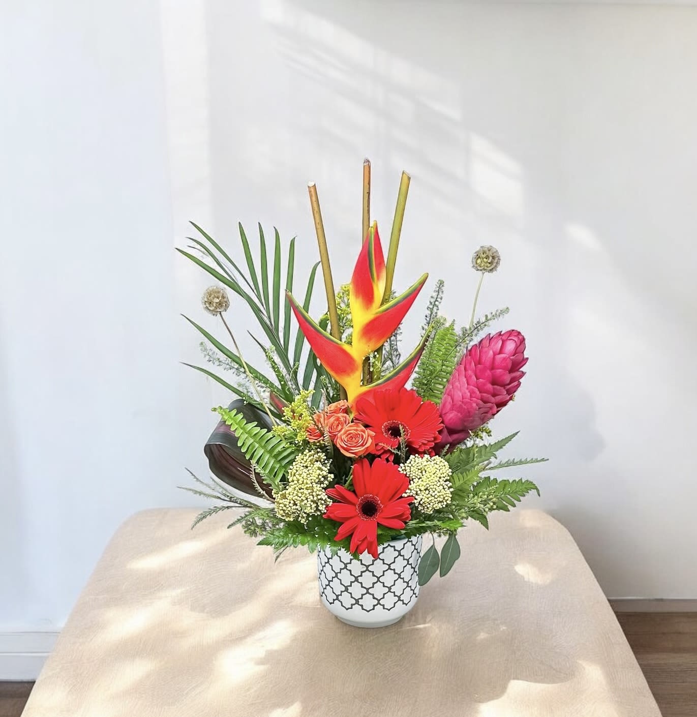 Tropical flower arrangement in a patterned white vase with red and pink blooms