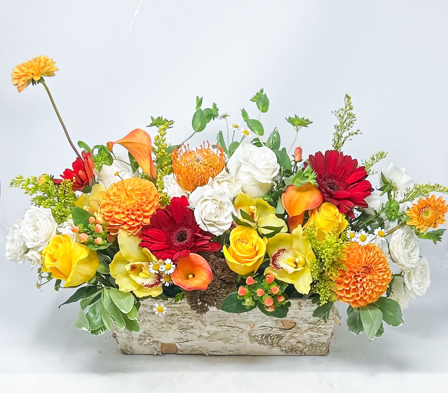 Mixed bouquet in a rustic rectangular wooden container with orange, yellow, red, and white flowers