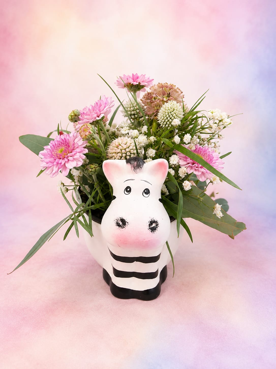 Pastel Pastures - Sweet, whimsical, and full of countryside charm, Pastel Pastures is arranged in an adorable zebra keepsake container and overflowing with soft pink daisy mums, delicate white blooms, airy greenery, and unique textural accents. Designed with a light, garden-inspired feel, this cheerful mini arrangement is perfect for celebrating birthdays, welcoming a new baby, saying thank you, or simply bringing a smile to someone's day. After the flowers are enjoyed, the playful zebra container becomes a keepsake that can be treasured for years to come.