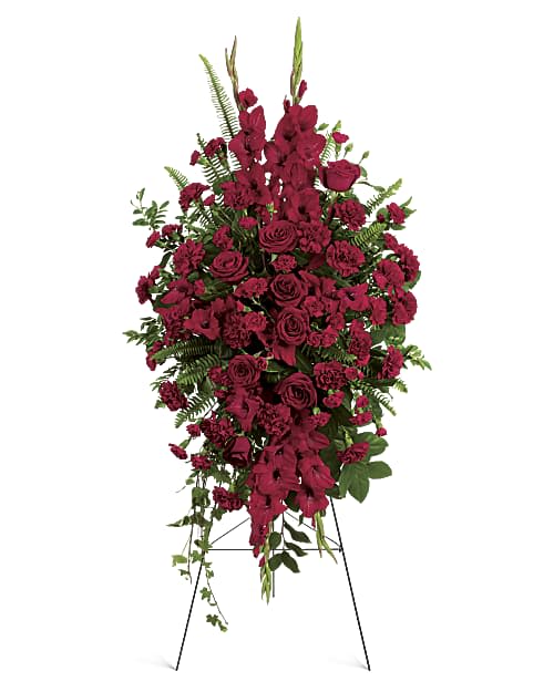 Crimson Legacy Standing Spray - The Crimson Legacy Standing Spray is a stunning tribute featuring rich crimson roses, carnations, and seasonal blooms accented with lush greenery. Displayed on an easel, this elegant arrangement offers a heartfelt expression of love, respect, and remembrance, creating a beautiful and lasting honor for a cherished life.