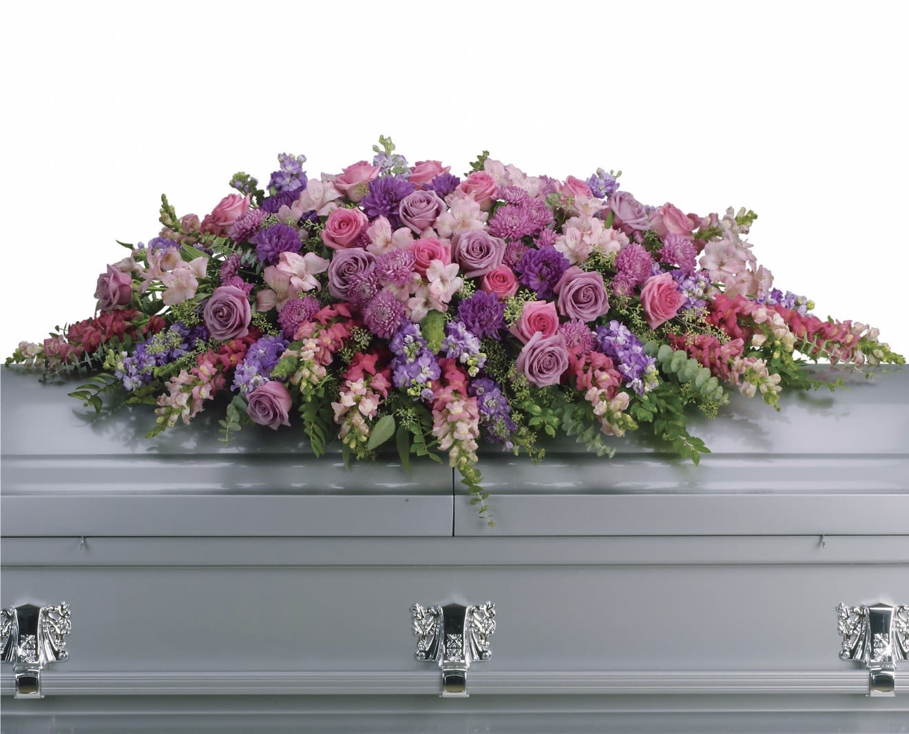 Lavender Tribute Casket Spray - Soft lavender and pink roses center this casket spray, their romantic hues paired with purple snapdragons, magenta accents, white chrysanthemums, and mixed carnations to create a gentle, feminine sympathy arrangement. As a casket spray for memorial services, it presents a full, layered surface that reads as both comforting and refined-an elegant way to honor someone cherished.  This large, low design is spread broadly across the casket with blooms cascading slightly over the edges for a formal, balanced presentation. Colors include pink, purple, white, and green foliage for texture; flowers shown include roses, carnations, snapdragons, chrysanthemums, and other mixed seasonal blooms to achieve a dense, graceful look. Suitable for funeral services or a memorial gathering, this spray arrives ready-to-display on a standard casket; if you need specific sizing or personalization, please contact us to confirm details.