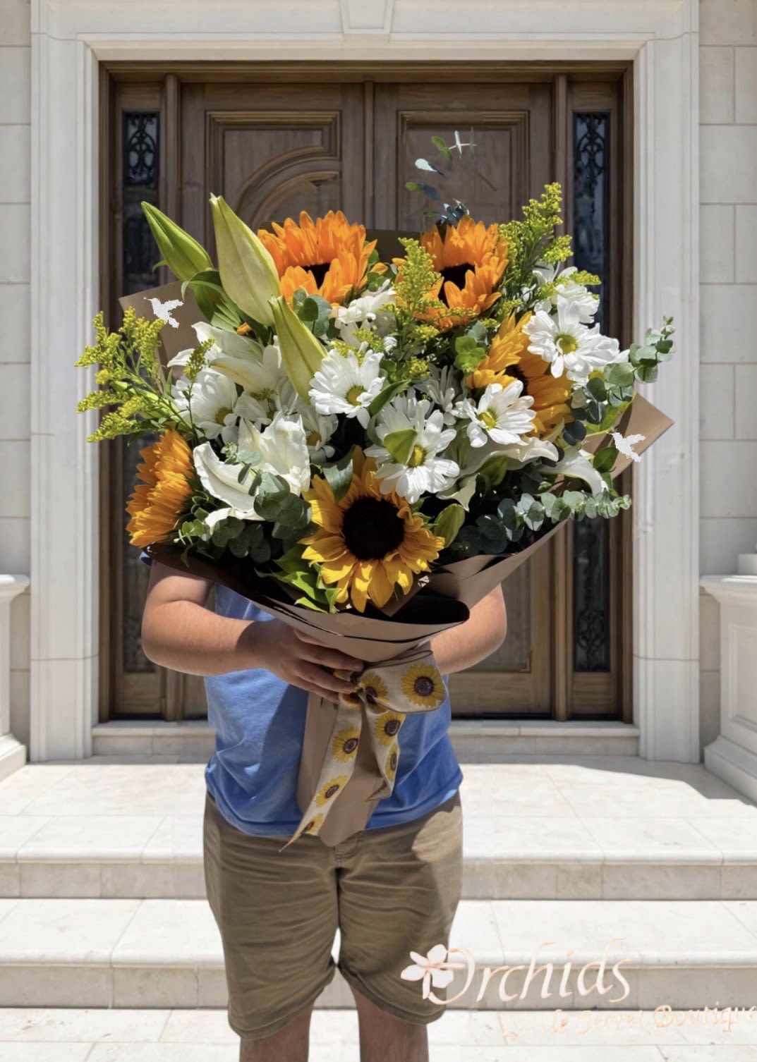 Sunflower &amp; Casablanca Lily Hand Wrapped  Bouquet - Bring warmth and elegance to any occasion with this beautifully handcrafted bouquet. Featuring vibrant sunflowers, fragrant white Casablanca lilies, cheerful white  daisies, delicate solidago, and fresh spiral eucalyptus, this arrangement is thoughtfully wrapped to create a stunning presentation. The combination of sunshine  blooms,  white flowers, and lush greenery makes it a perfect gift for birthdays, celebrations, thank-you gifts, housewarmings, or simply to brighten someone's day.  