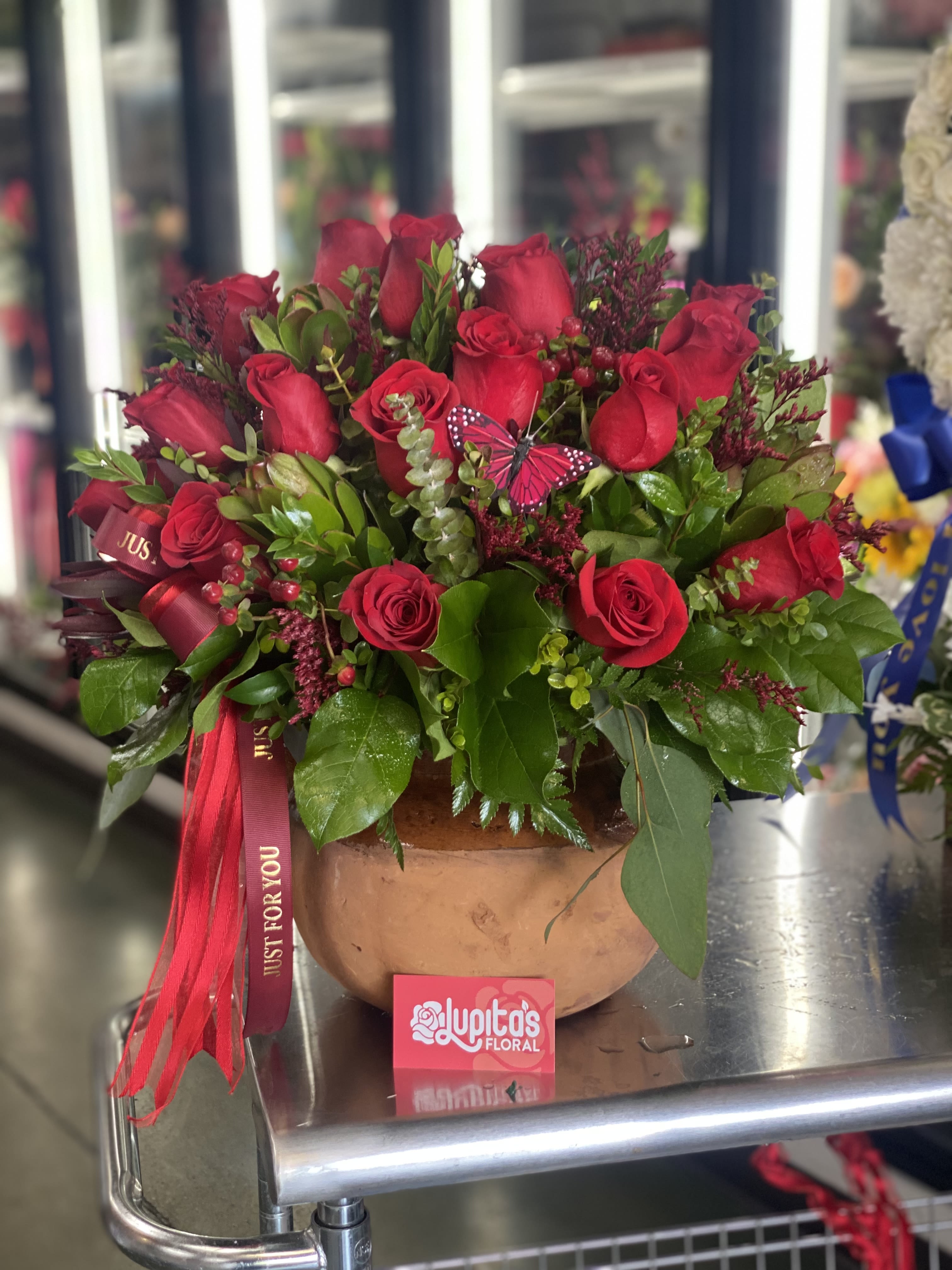 Red roses arranged in a round terracotta pot with a ribbon.