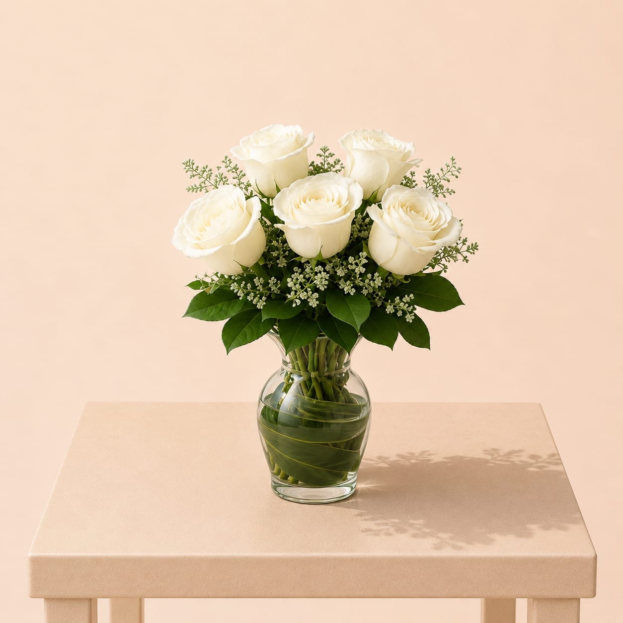 White roses arranged in a clear glass vase with greenery