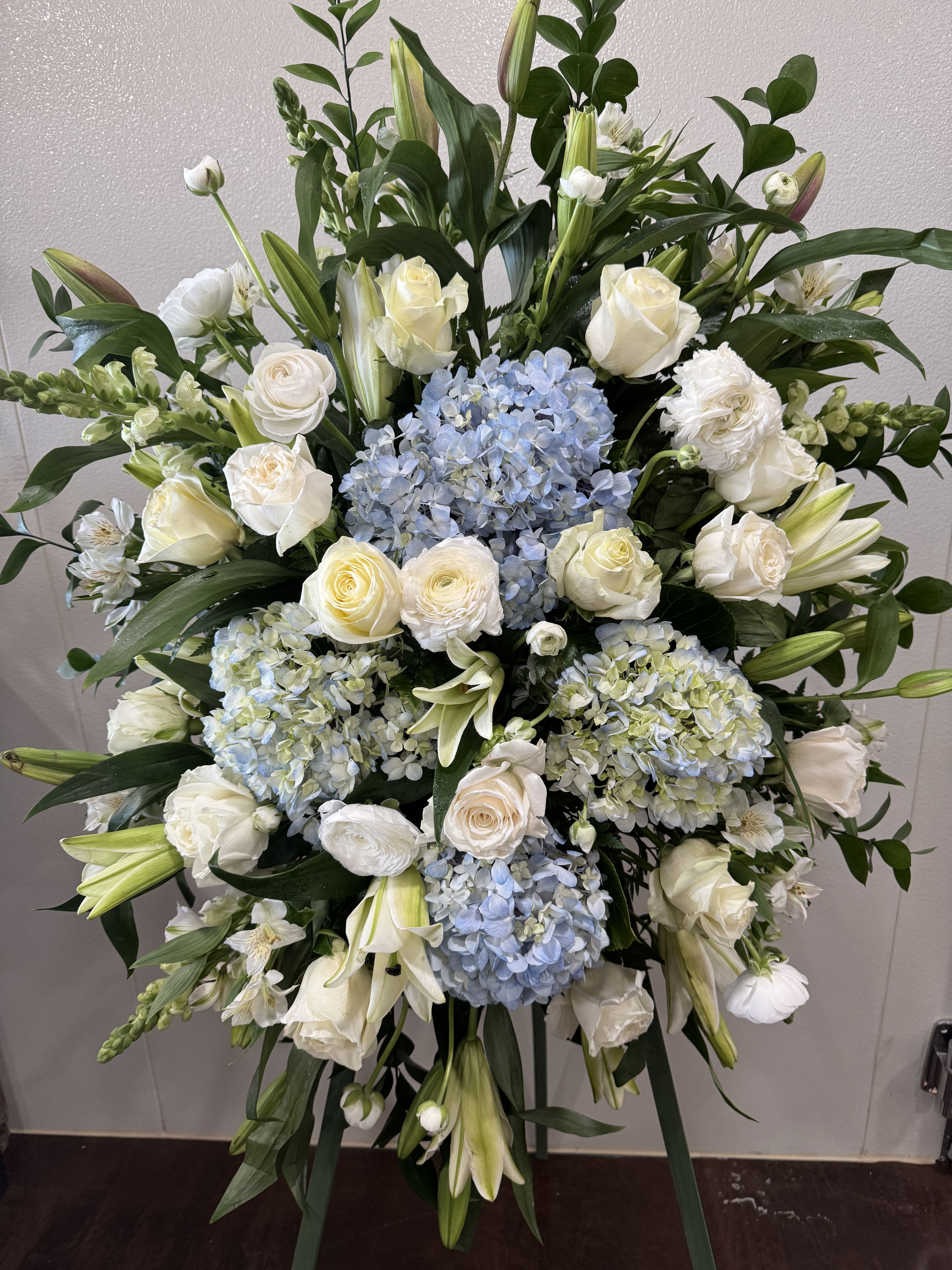 Large standing floral spray with white roses, lilies, and blue hydrangeas