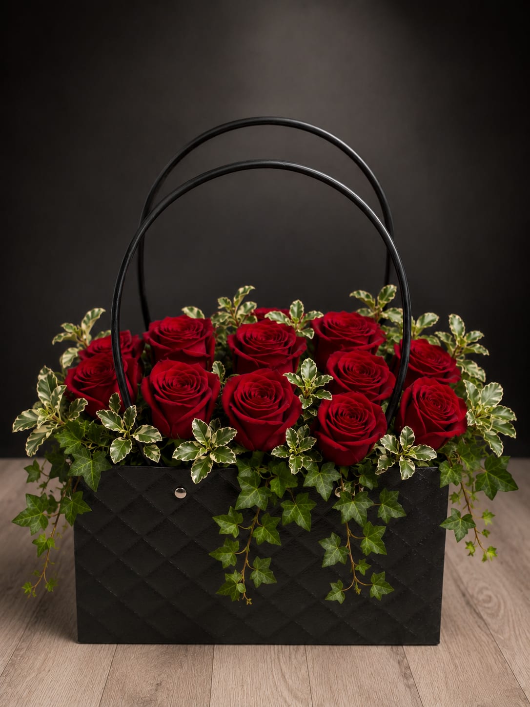 Eternal Passion - A dense cluster of deep red roses packed tightly into a black quilted basket creates an unforgettable romantic statement-perfect as a birthday bouquet for a partner, an anniversary roses gift, or a Valentine's arrangement. The dramatic red-and-black contrast reads formal and luxurious, so the person you're thinking of will feel deeply celebrated the moment they see it.  The arrangement sits low in a black basket with a tall arched handle, the quilted texture adding a couture touch. Variegated and trailing ivy spill over the edges, introducing soft green and white highlights that temper the intensity of the roses and create a layered, garden-like cascade. The compact, sculpted shape and polished presentation make this an elegant choice for love-themed, celebratory, or formal occasions; order with standard care instructions for fresh-cut roses and keep in a cool spot away from direct sun for best longevity.