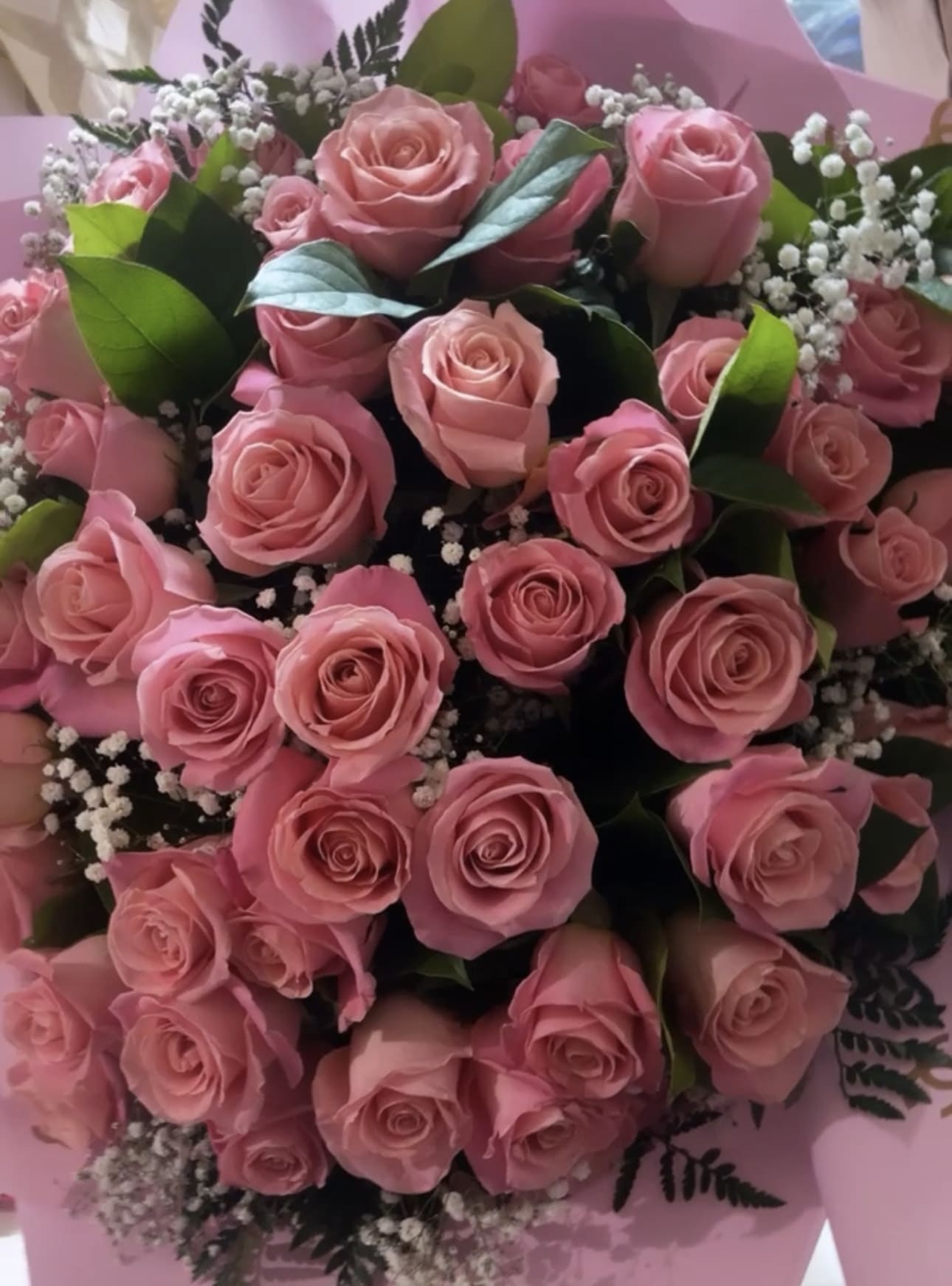 Large bouquet of pink roses with white baby's breath accents in pink wrapping paper
