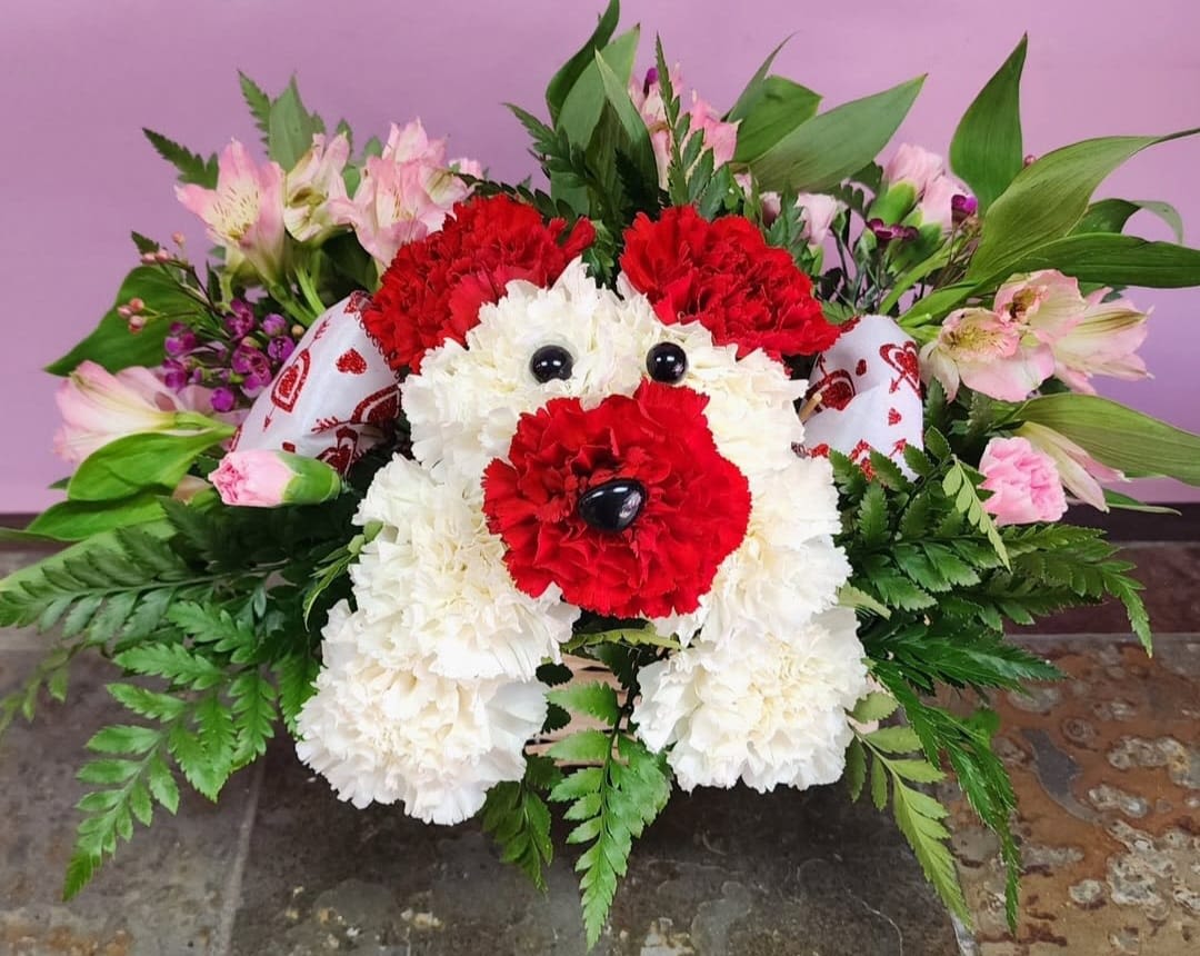 Dog-shaped floral arrangement made of red and white carnations with pink flowers around it