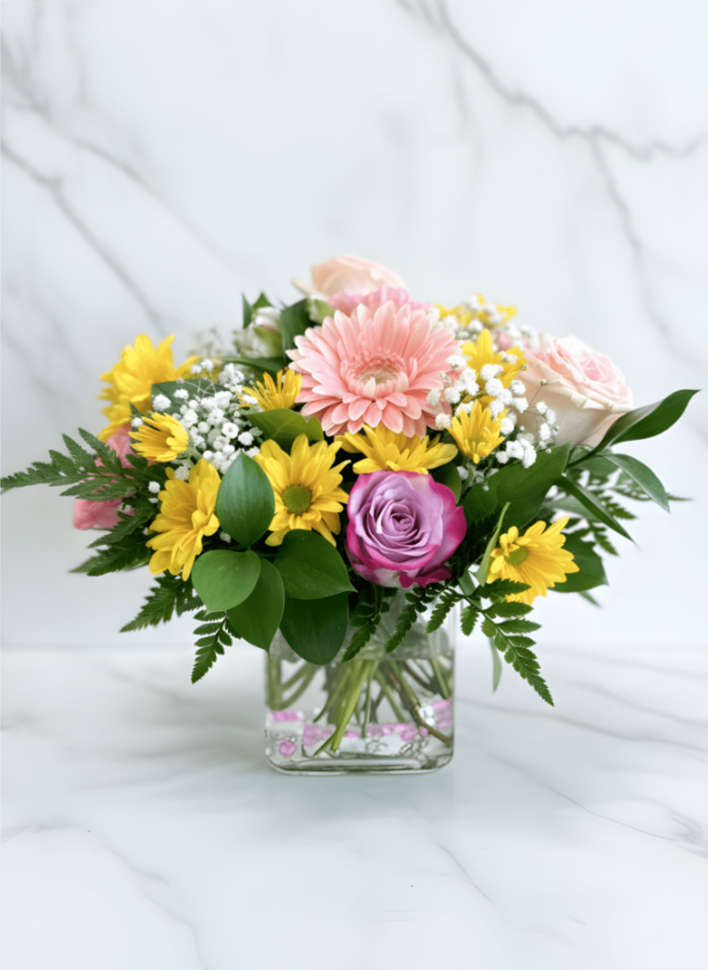  Floral Melody - Bring warmth and happiness to any occasion with Floral Melody, a vibrant floral arrangement artfully designed in a modern low glass cube vase. Featuring soft pink gerbera daisies, lavender and blush roses, cheerful yellow daisies, delicate baby's breath, and fresh greenery, this elegant bouquet is perfect for birthdays, anniversaries, Mother's Day, congratulations, thank-you gifts, get well wishes, new baby celebrations, or just because. Handcrafted with fresh flowers, it's a beautiful gift that delivers smiles for every special moment.