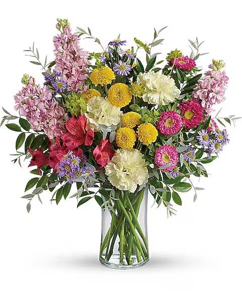 Goodness And Light Bouquet - A cheerful, garden-style bouquet that feels like sunshine in a vase - the Goodness And Light flower arrangement is a bright everyday bouquet perfect for birthdays, thank-you gestures, or spring celebrations. The rounded, full composition mixes pinks, creamy whites, sunny yellows and pops of purple so the person you're sending it to immediately feels noticed and uplifted.  This arrangement blends ruffled carnations and creamy roses with alstroemeria and chrysanthemum blooms, finished with purple aster and daisy-like accents for a lively, layered texture. An airy touch of branching greenery and button-style yellow mums add contrast and movement, while the clear glass vase keeps the look clean and classic. The balanced heights and dense, garden-inspired styling make the bouquet feel abundant without being fussy.  Ideal for brightening someone's day - whether celebrating a birthday, saying thanks, or welcoming spring - this bouquet arrives ready to display in a clear glass vase. For best enjoyment, change the water every few days, trim stems at an angle, and keep the arrangement out of direct heat to help the recipient enjoy its colors and fragrance longer.
