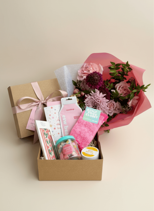 Pink flower bouquet beside a gift box filled with small packaged items