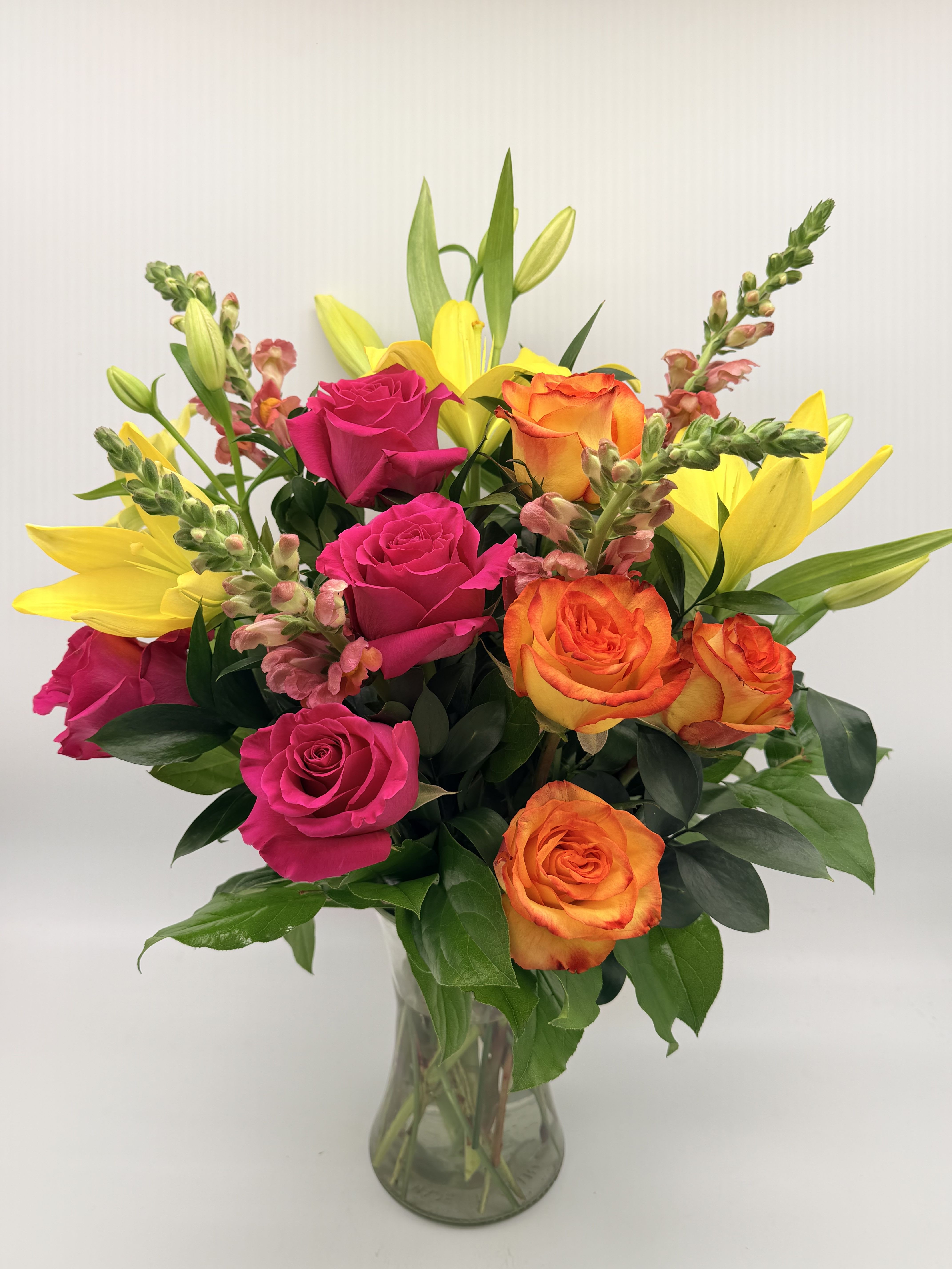 Bouquet of pink and orange roses with yellow lilies in a glass vase