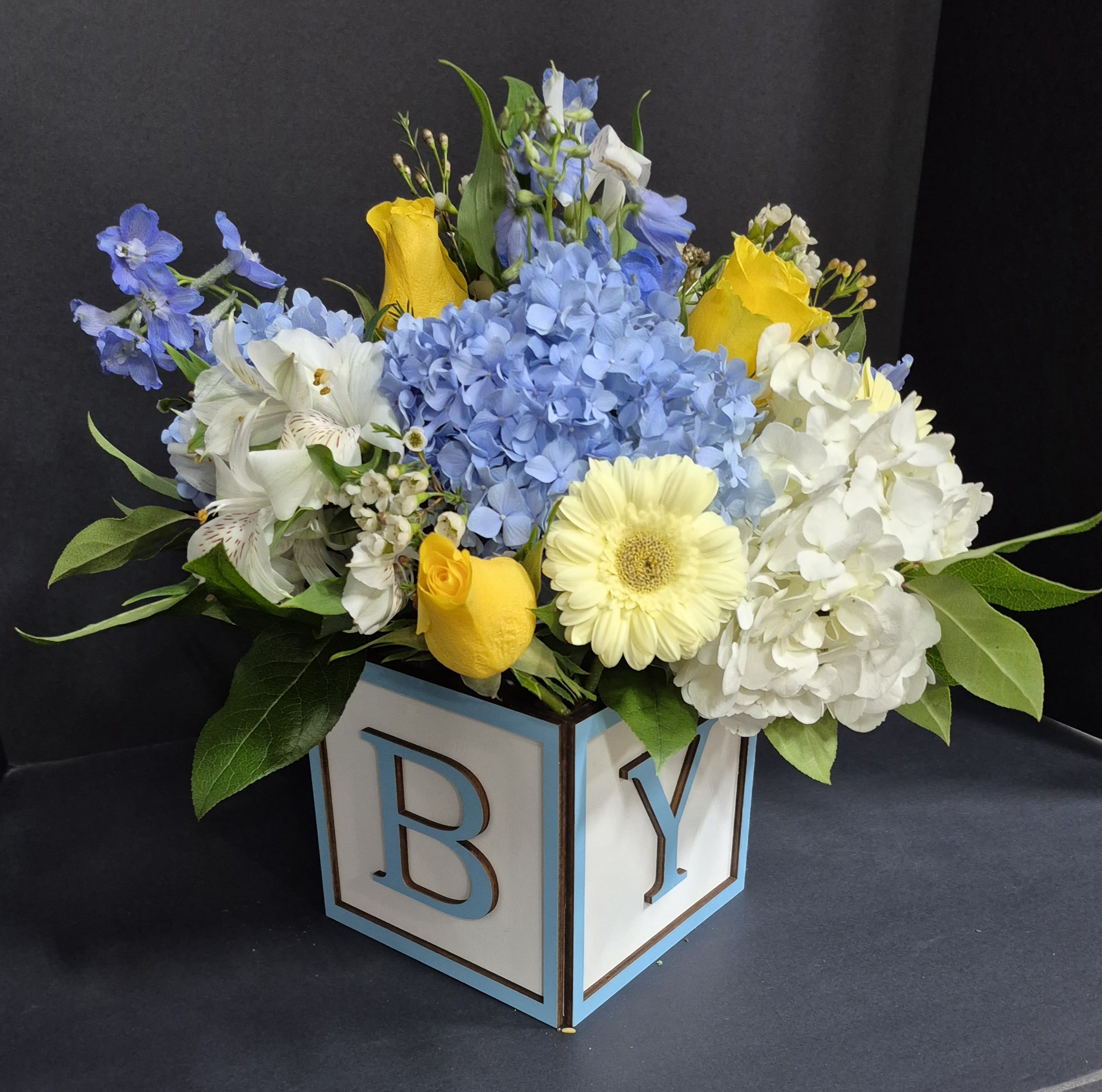 Blossoming Baby Boy Blue - Beautiful seasonal flowers in a blue trimmed 6" wooden block that spells out "BABY."  An adorable and elegant way to welcome a new bundle of joy!   Call us if you have any other specific colors in mind.  Deluxe size pictured.