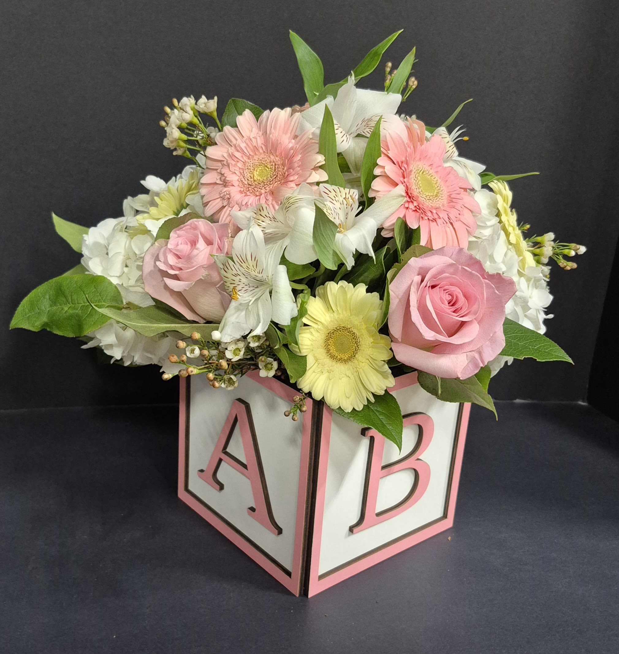 Precious Baby Girl Pink - Beautiful seasonal flowers in a pink trimmed 6" wooden block that spells out "BABY."  An adorable and elegant way to welcome a new bundle of joy!   Call us if you have any other specific colors in mind.  Deluxe size pictured.