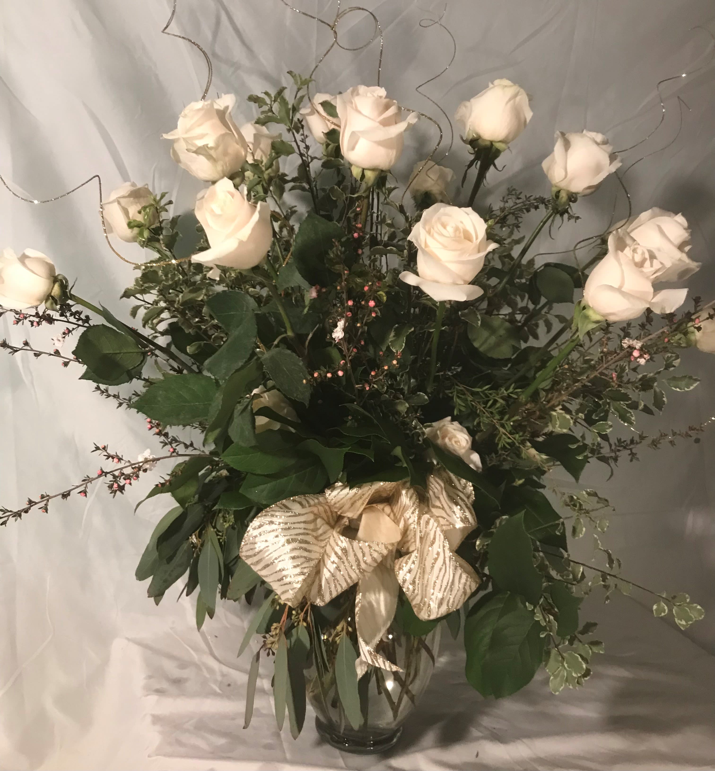 White roses in a clear glass vase with a gold ribbon bow