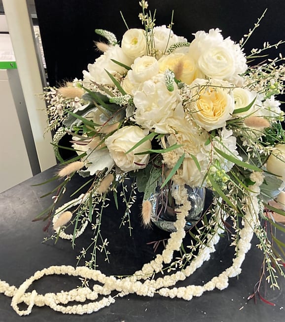 Cream and white floral arrangement in a glass vase with trailing accents