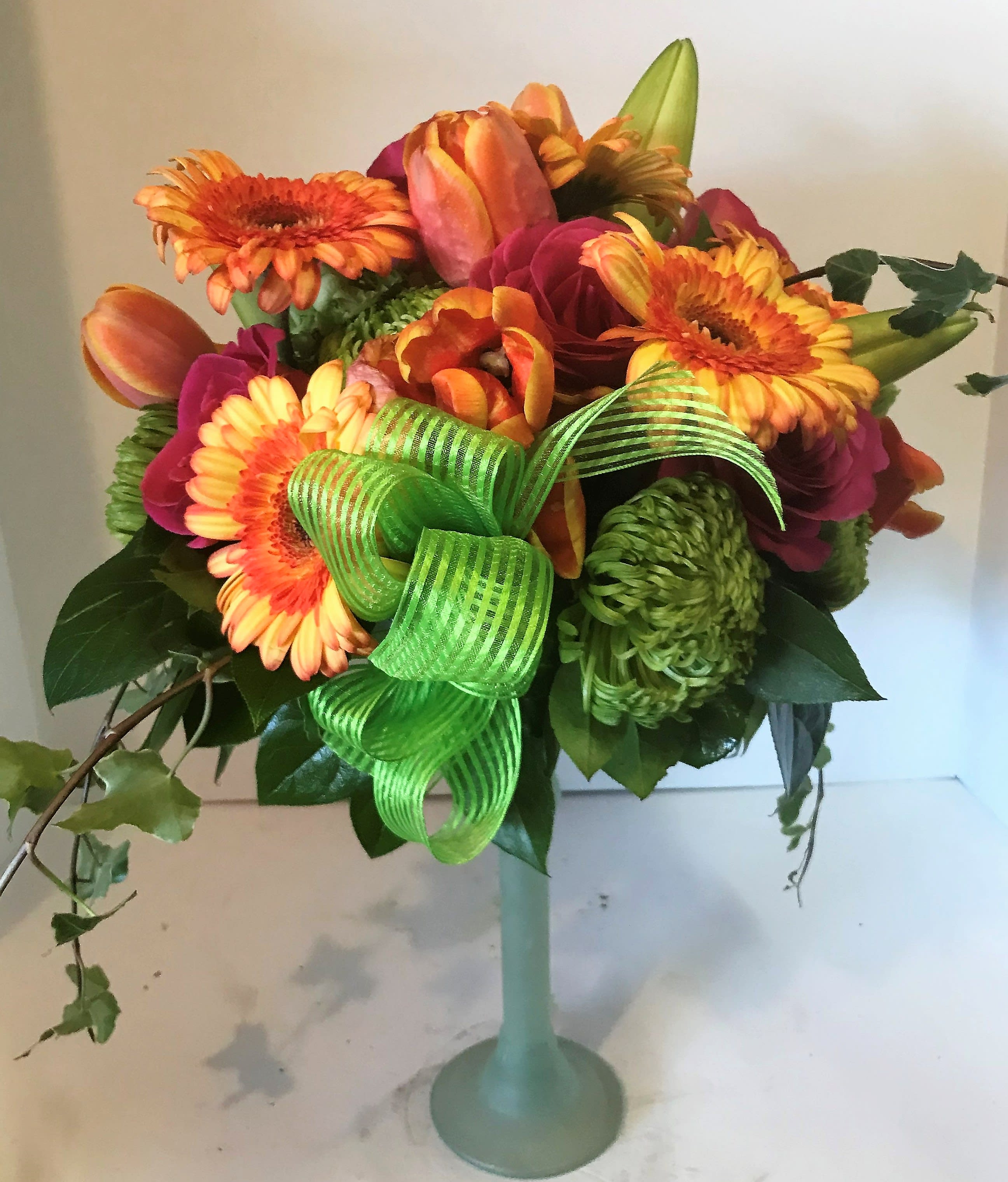 Bouquet of orange and pink flowers in a tall glass vase with a green ribbon