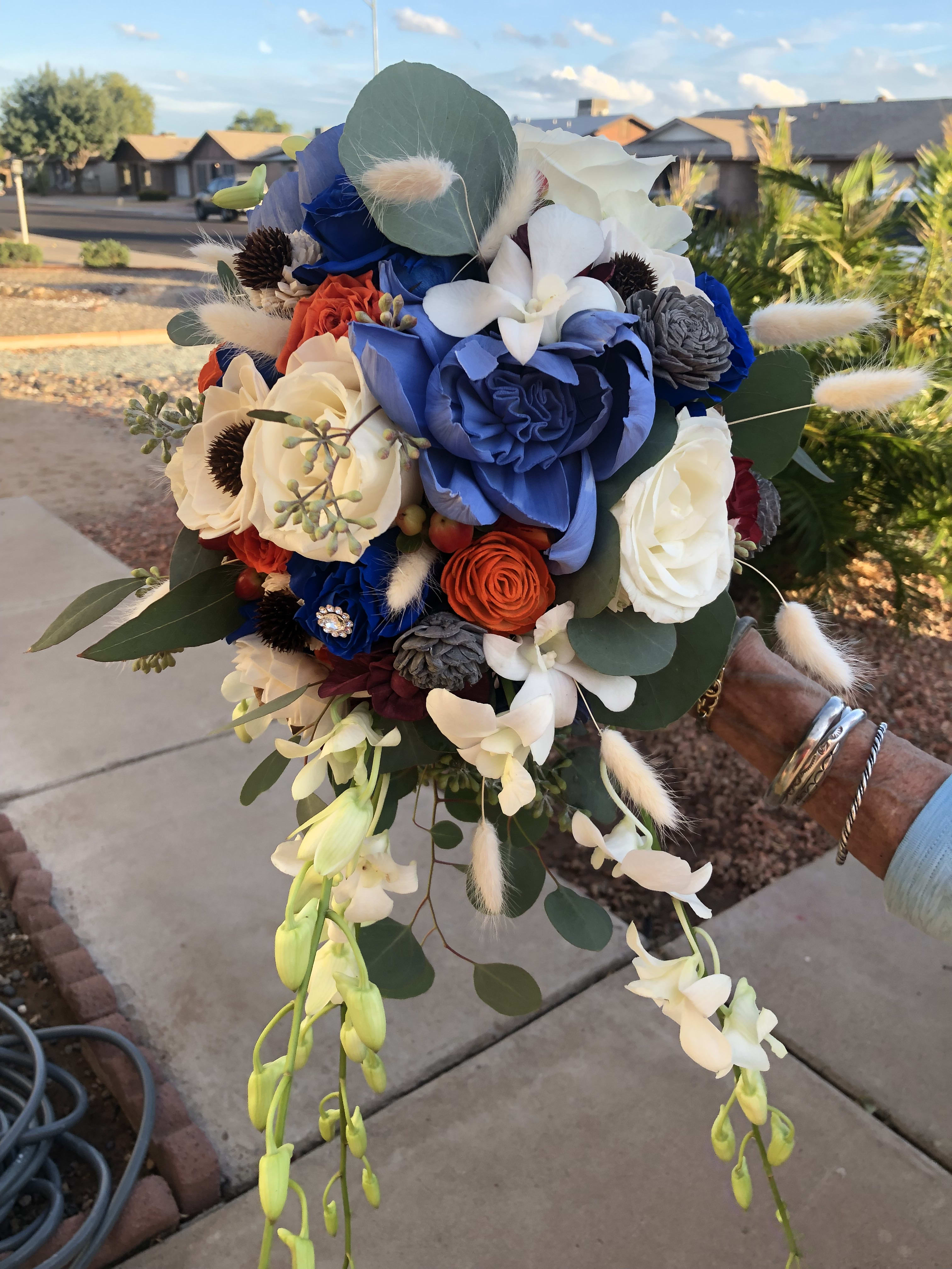 Handheld bouquet with blue, white, and orange flowers and trailing orchids