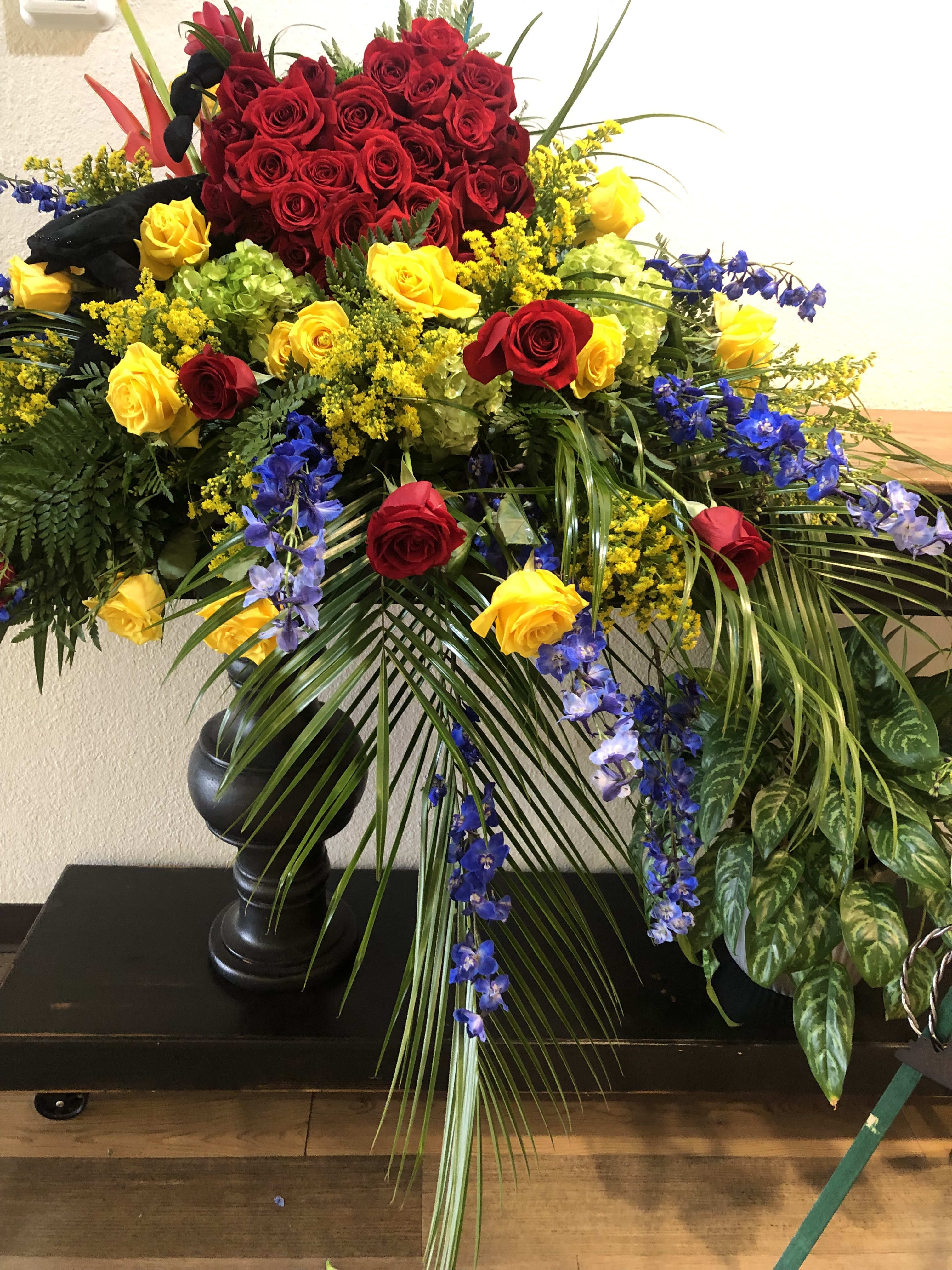 Large standing arrangement of red and yellow roses with blue flowers in a black vase