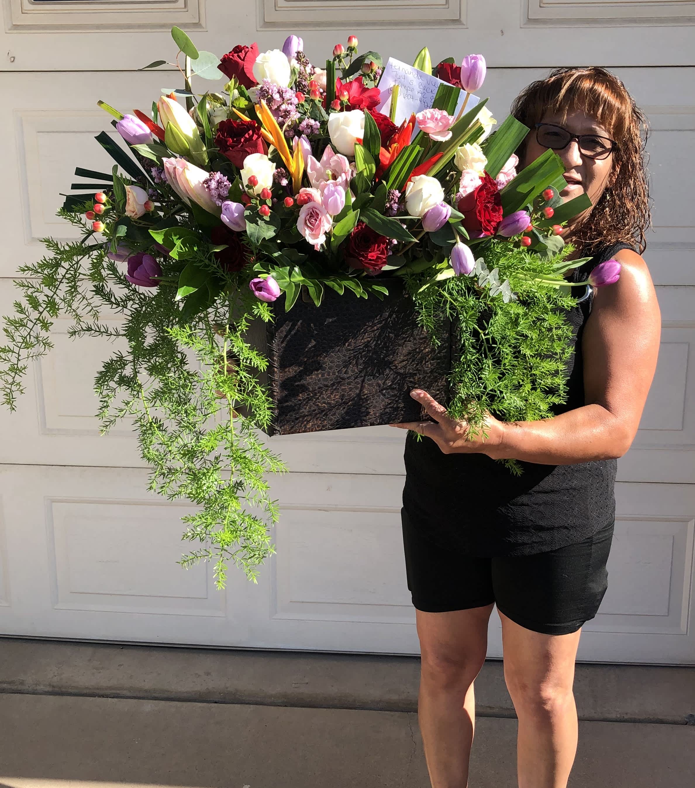 Large mixed flower arrangement in a black container held by a woman
