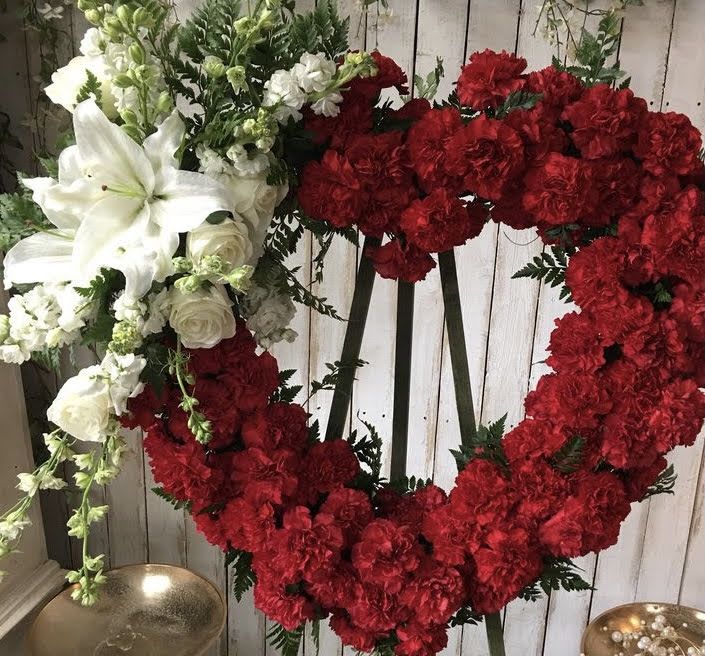 Heart-shaped floral wreath with red and white flowers on a stand