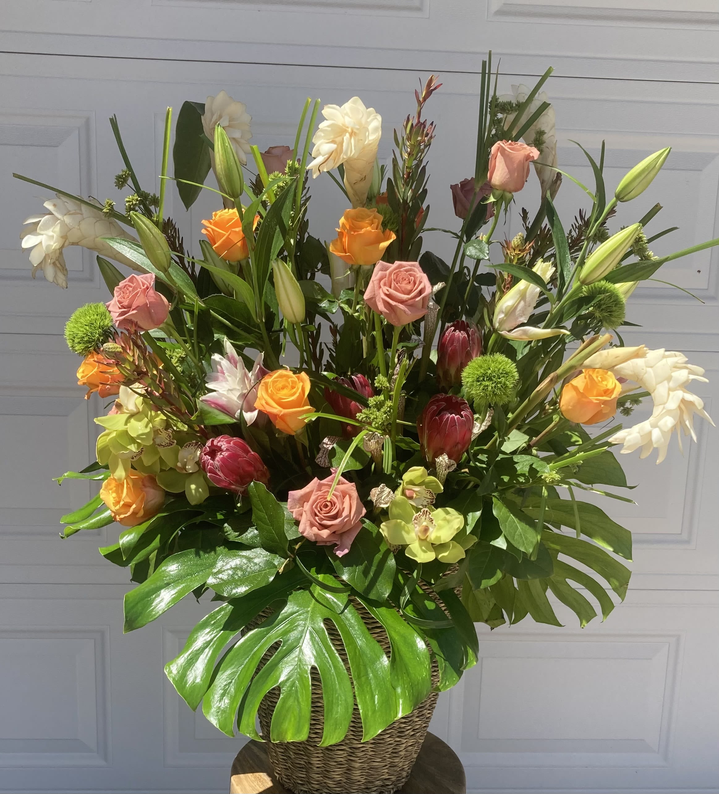 BOBBY'S BLUE SKIES - AN EXTRA LARGE TROPICAL FLORAL ARRANGEMENT, PERFECT TO CLEAR AWAY THE SHOWERS AND FORGE AHEAD WITH BLUE SKIES. THIS ARRANGEMENT IS FILLED WITH WHITE GINGER, ROSES, TROPICAL GREENS, COBRA LILIES, ORIENTAL LILIES AND PROTEAS.