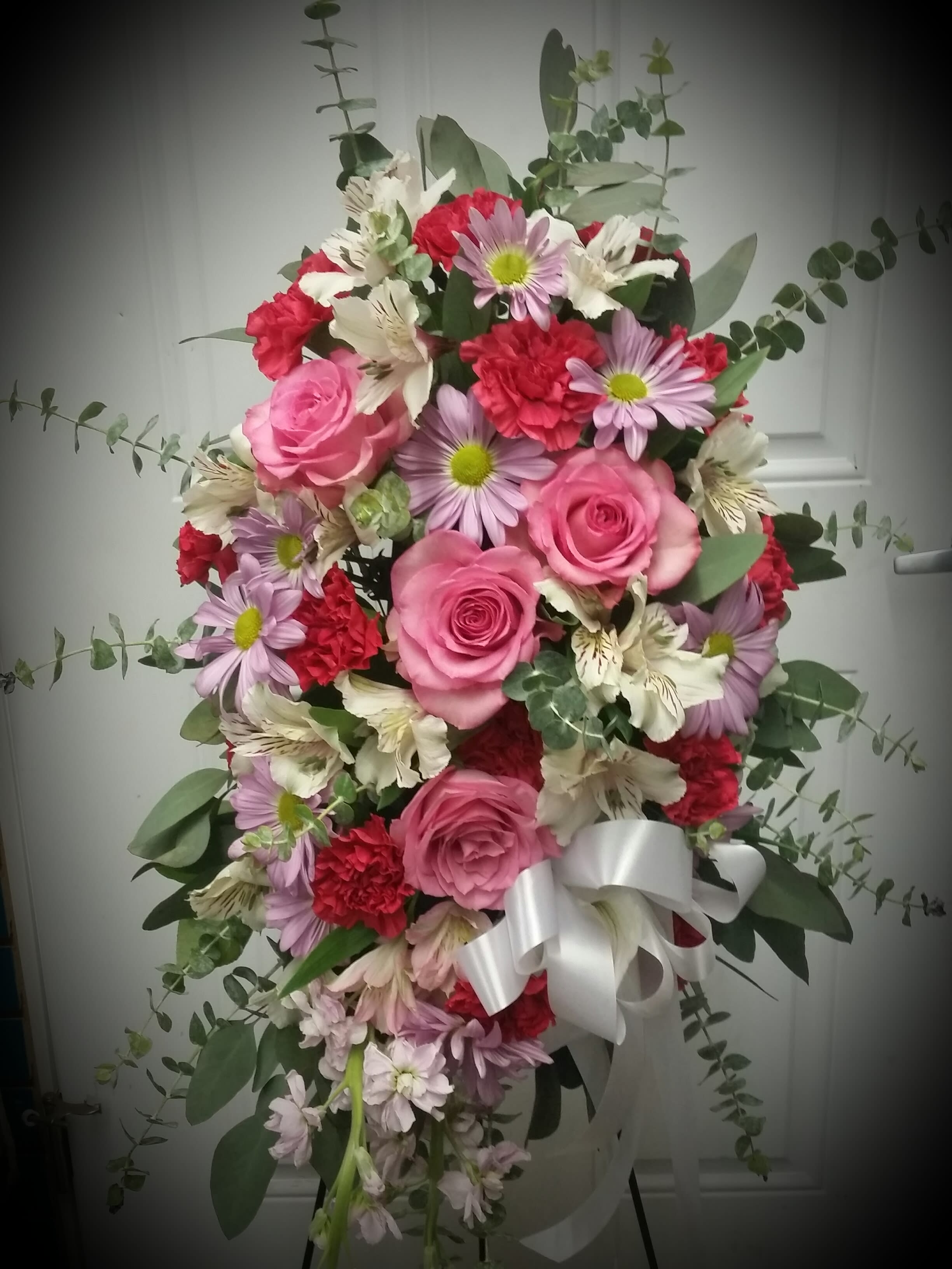 Pink and red mixed flower arrangement with a white ribbon