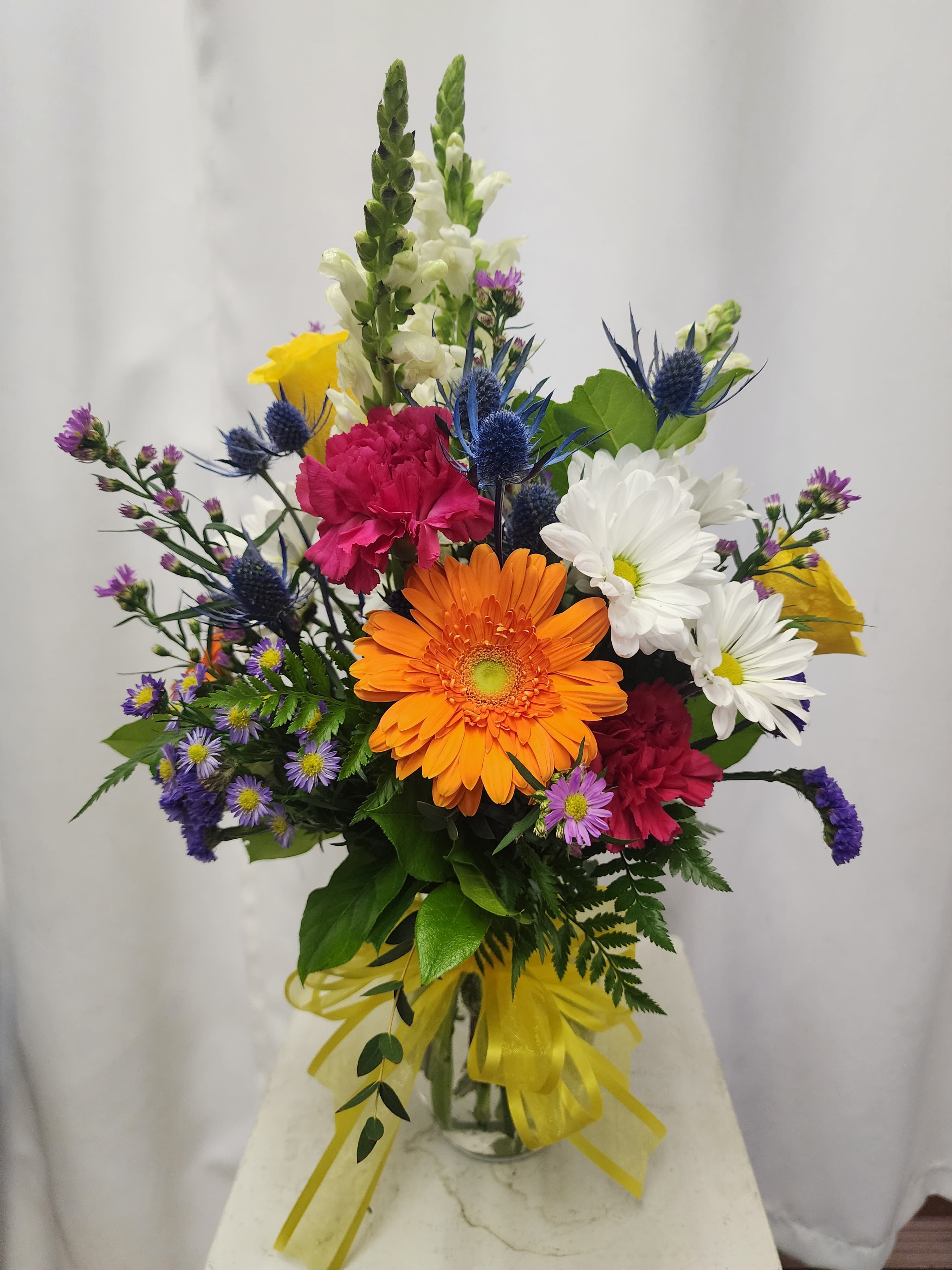 Mixed bouquet with orange gerbera daisies, white daisies, and pink carnations in a glass vase