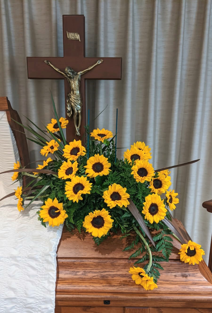 Sunflower arrangement displayed beside a wooden cross on a casket