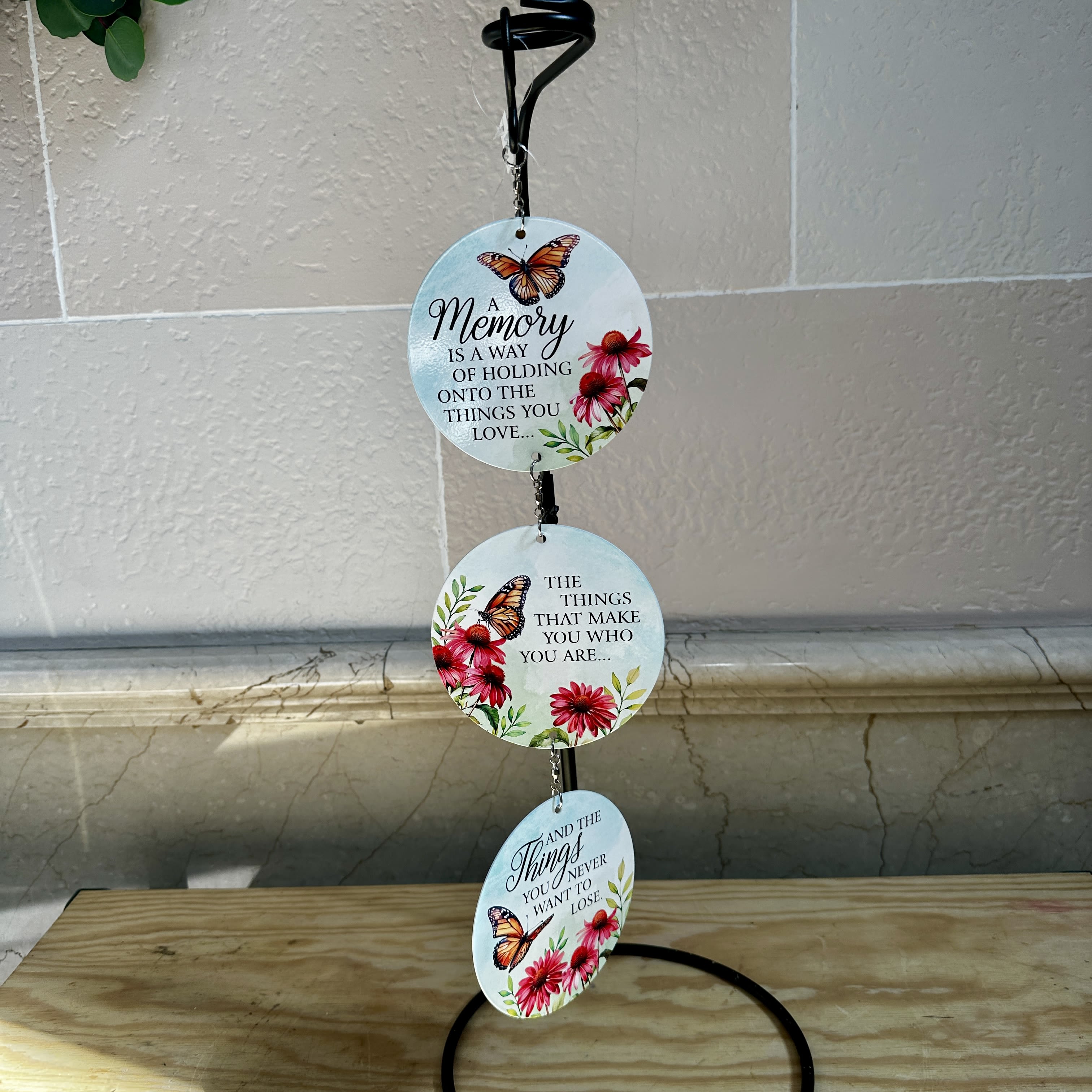 Three round memorial plaques hang from a black stand with butterfly and flower designs.