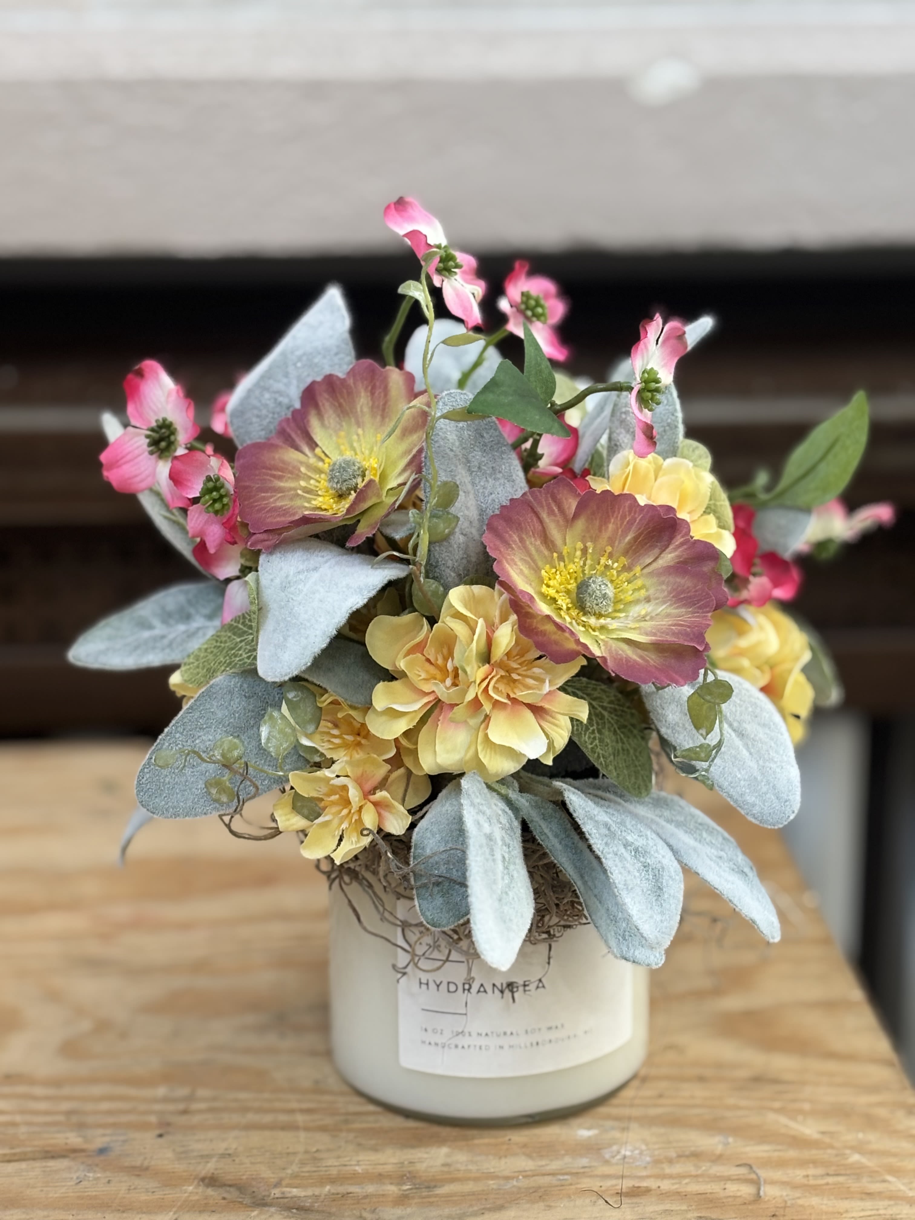 Small floral arrangement in a white container with pink and yellow blooms