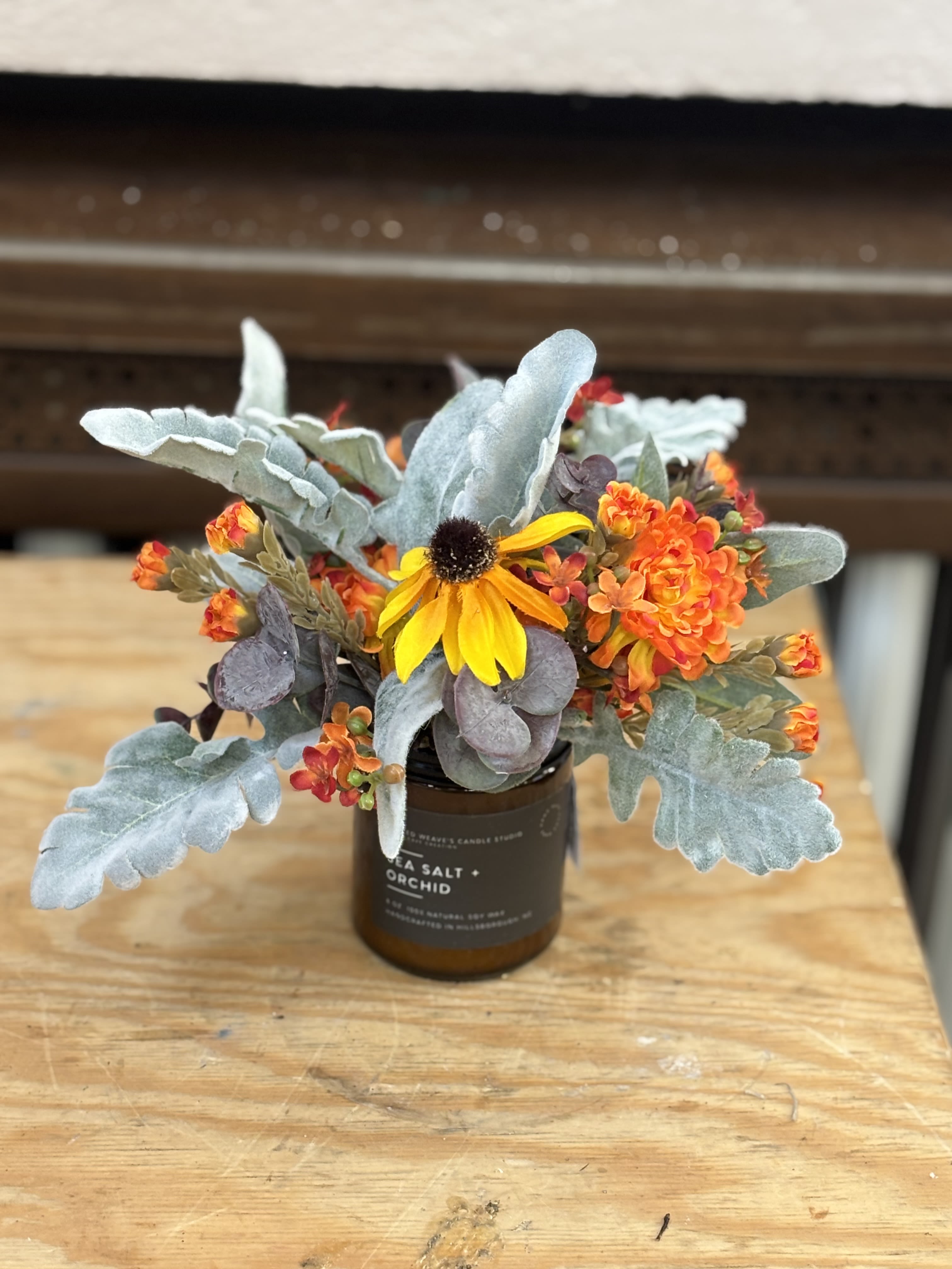 Small floral arrangement in a brown candle jar with yellow and orange blooms