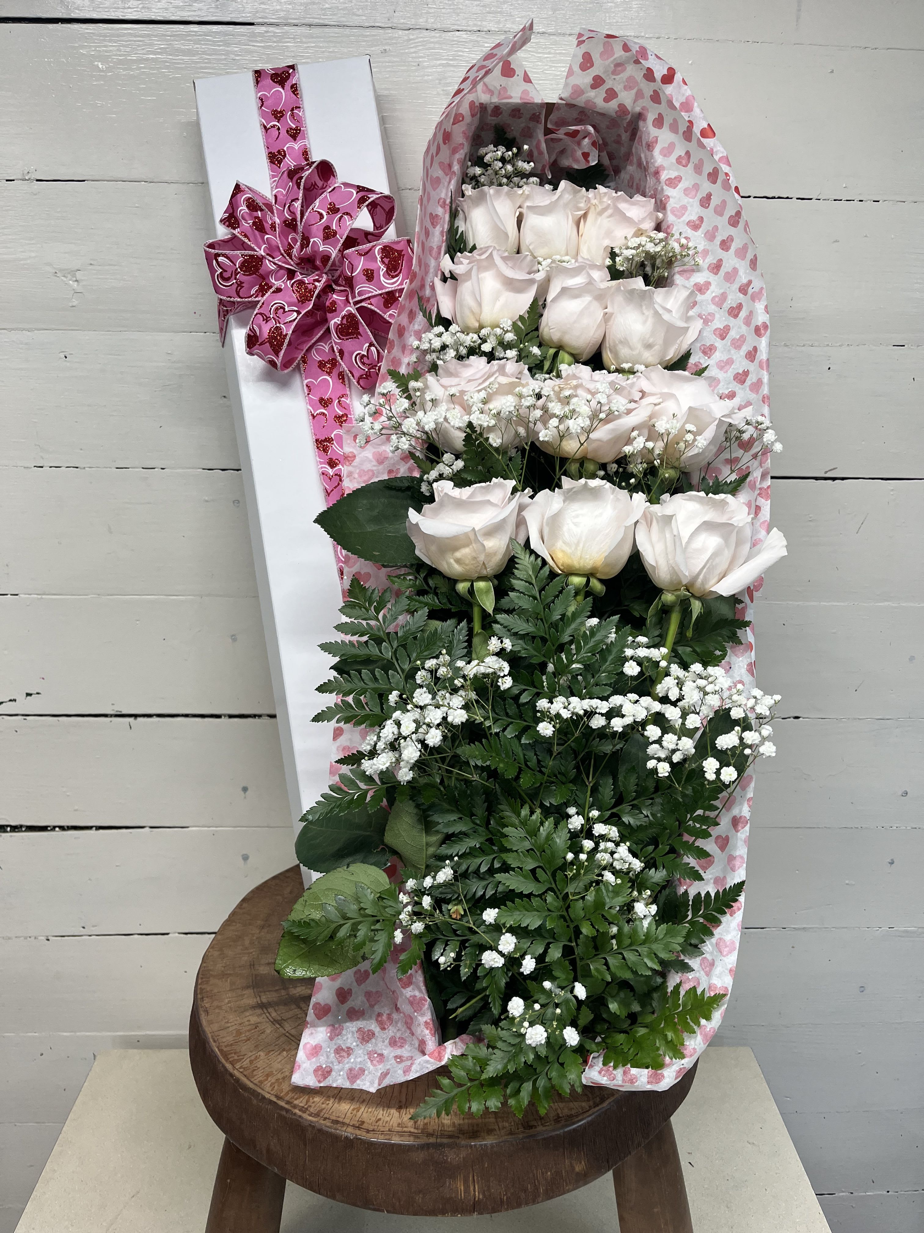 Bouquet of pale pink roses wrapped in heart-patterned paper with a pink bow