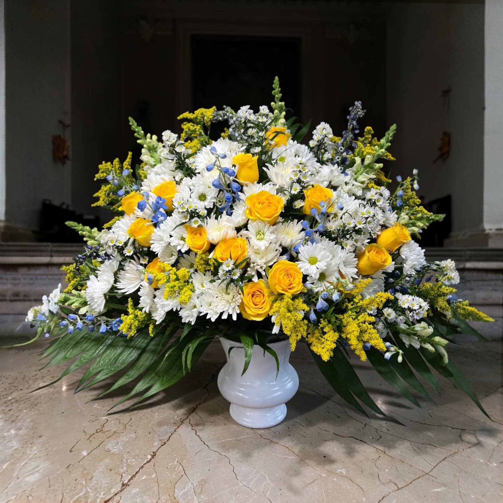 Deepest Condolences - A sophisticated memorial arrangement held in a large white urn with wide-spread palms giving a natural spotlight for the feature blooms and colors.