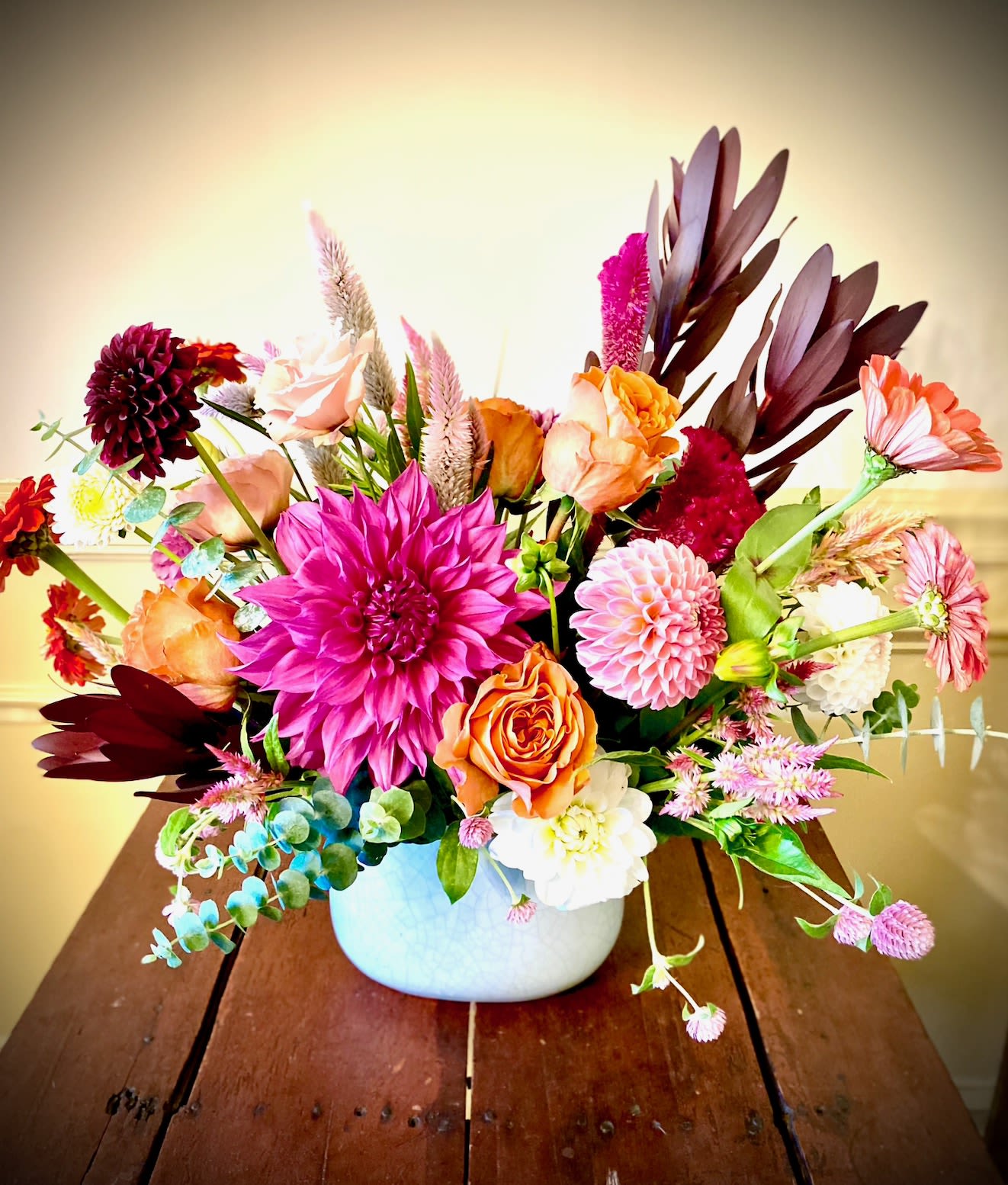 Bright mixed arrangement of pink dahlias, orange roses, and assorted blooms in a white ceramic bowl vase.