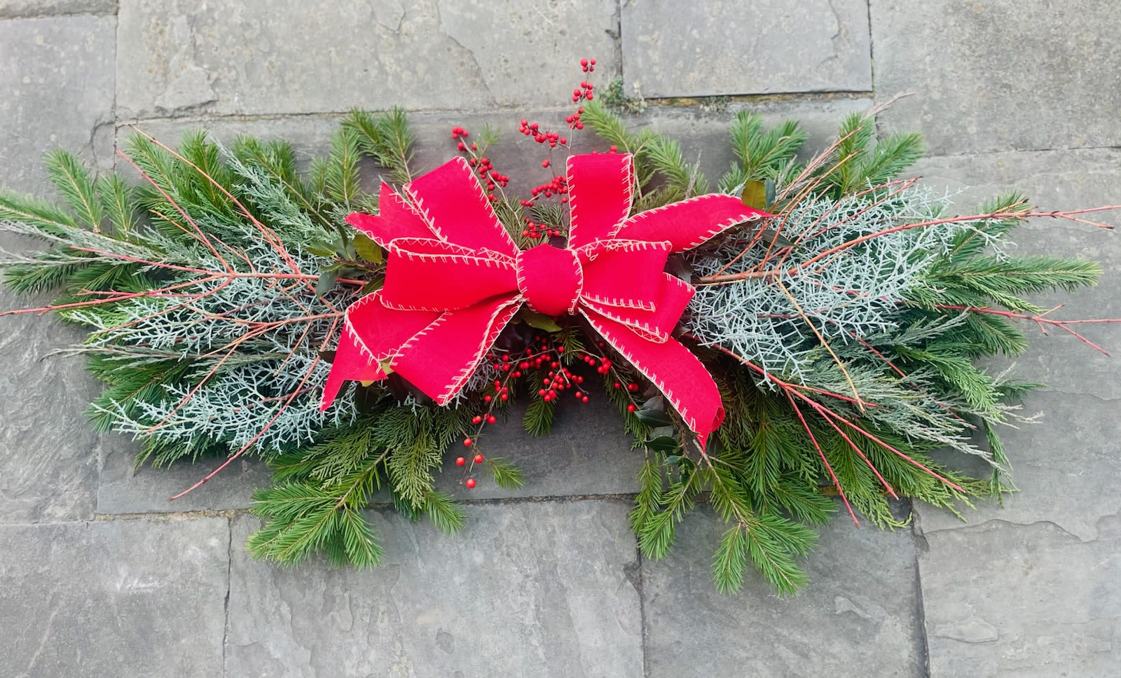 Evergreen swag with red berries and a large red bow on a stone surface
